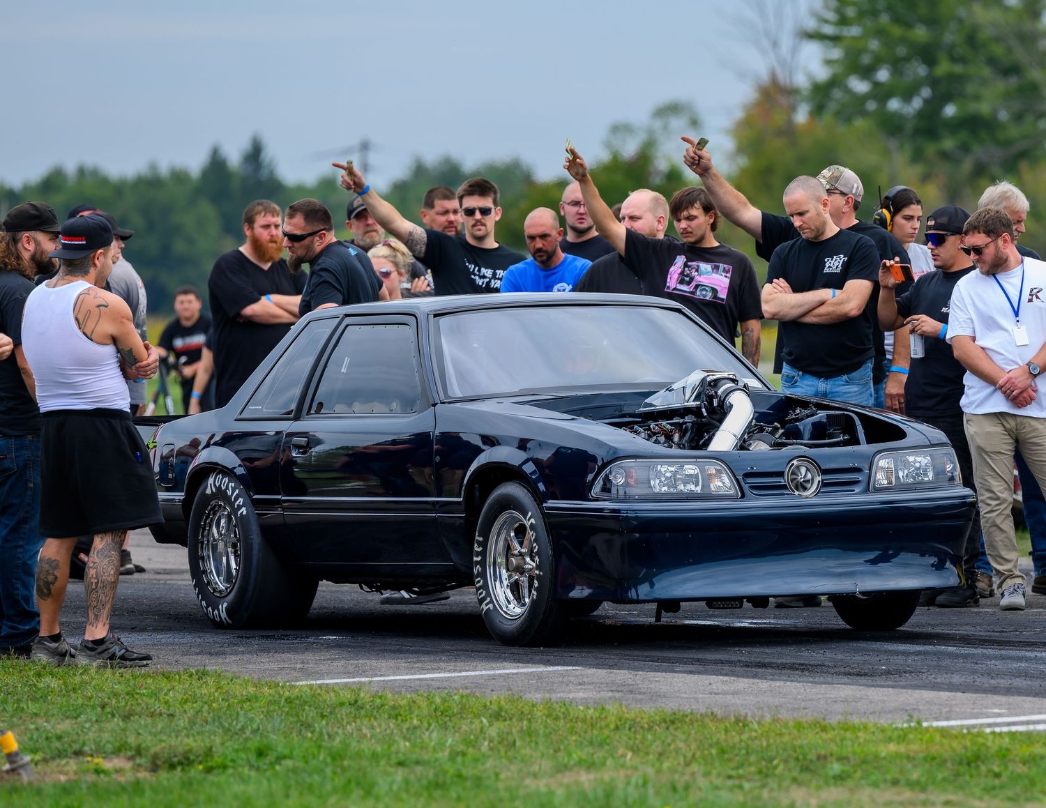 Black sports cars lined up at a car meet performing burnouts on an outdoor track.