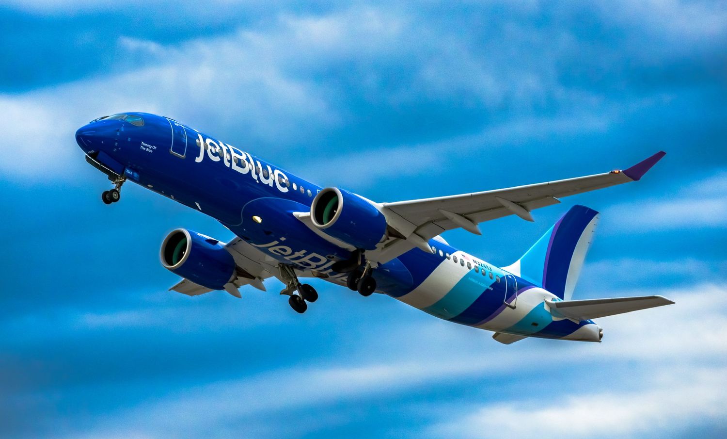 JetBlue Airways blue Boeing aircraft soaring through dramatic cloudy sky during flight.