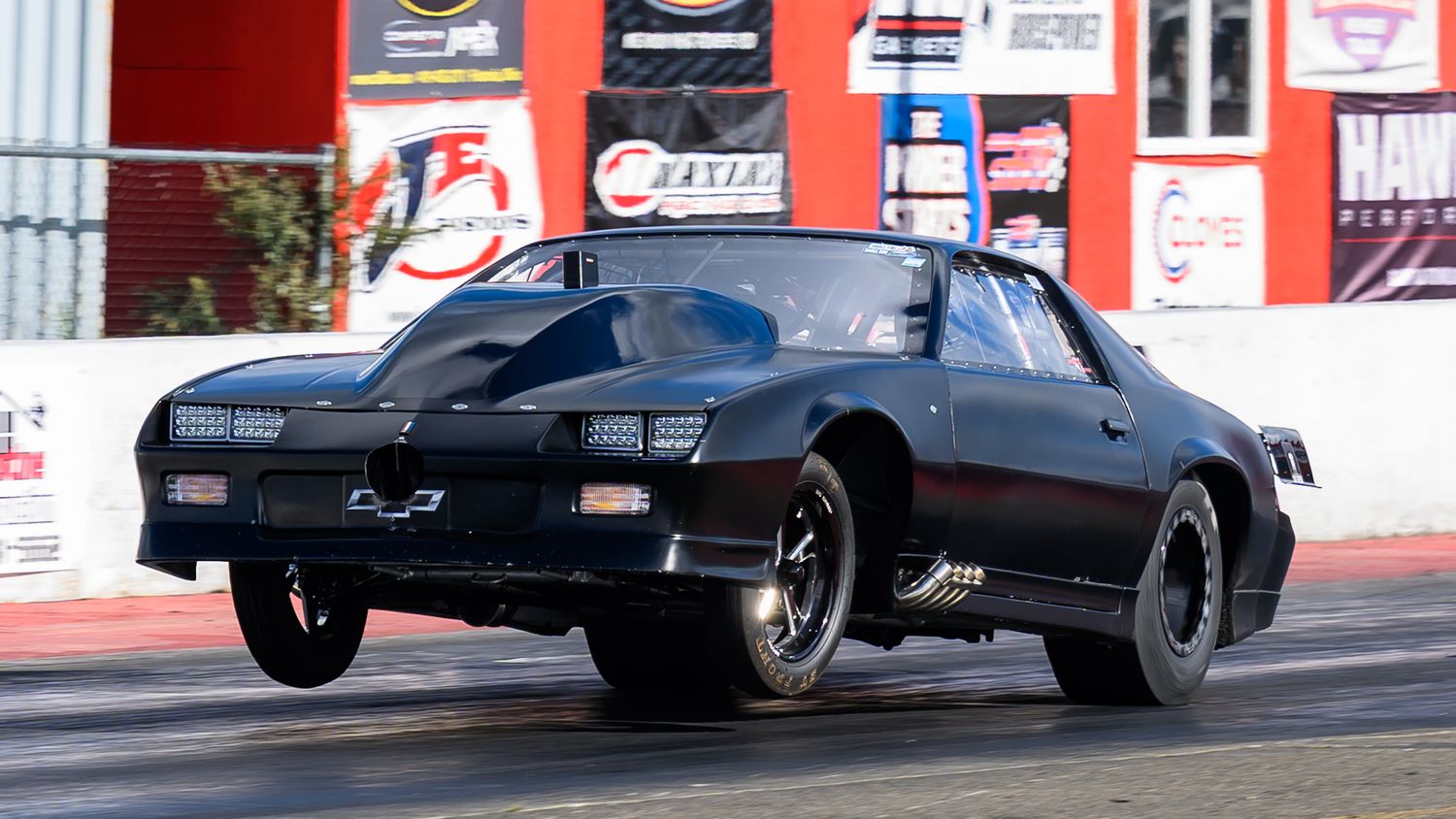 Drag racing cars speeding down a track with smoke trailing behind them.