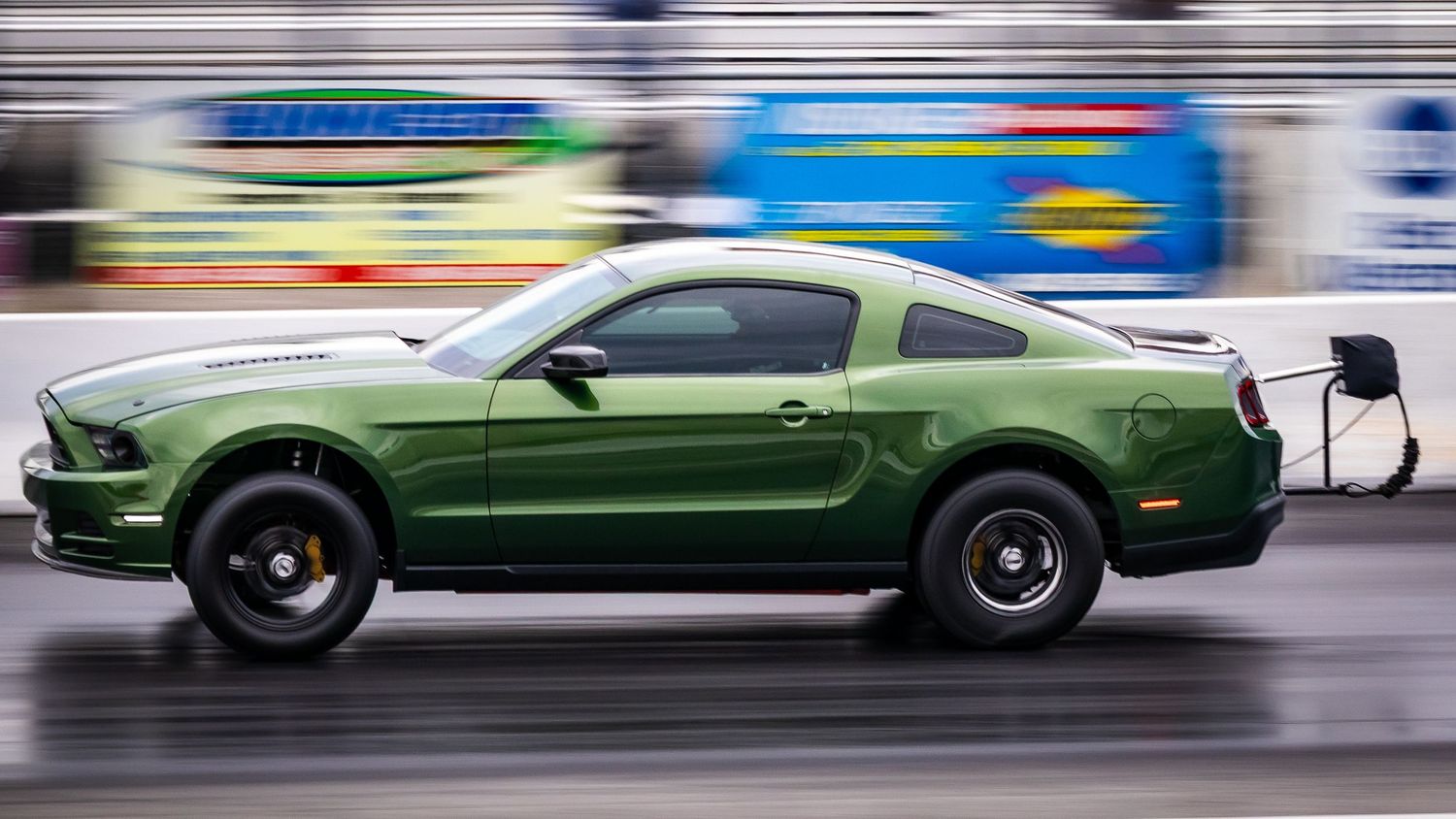 Green and white muscle cars racing down drag strip with motion blur.