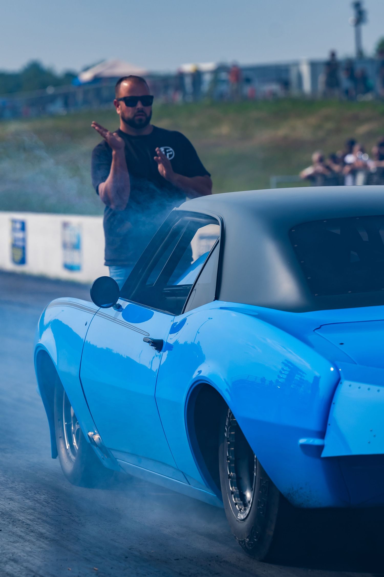 A blue drag racing car performing a burnout with smoke trailing behind on the track.