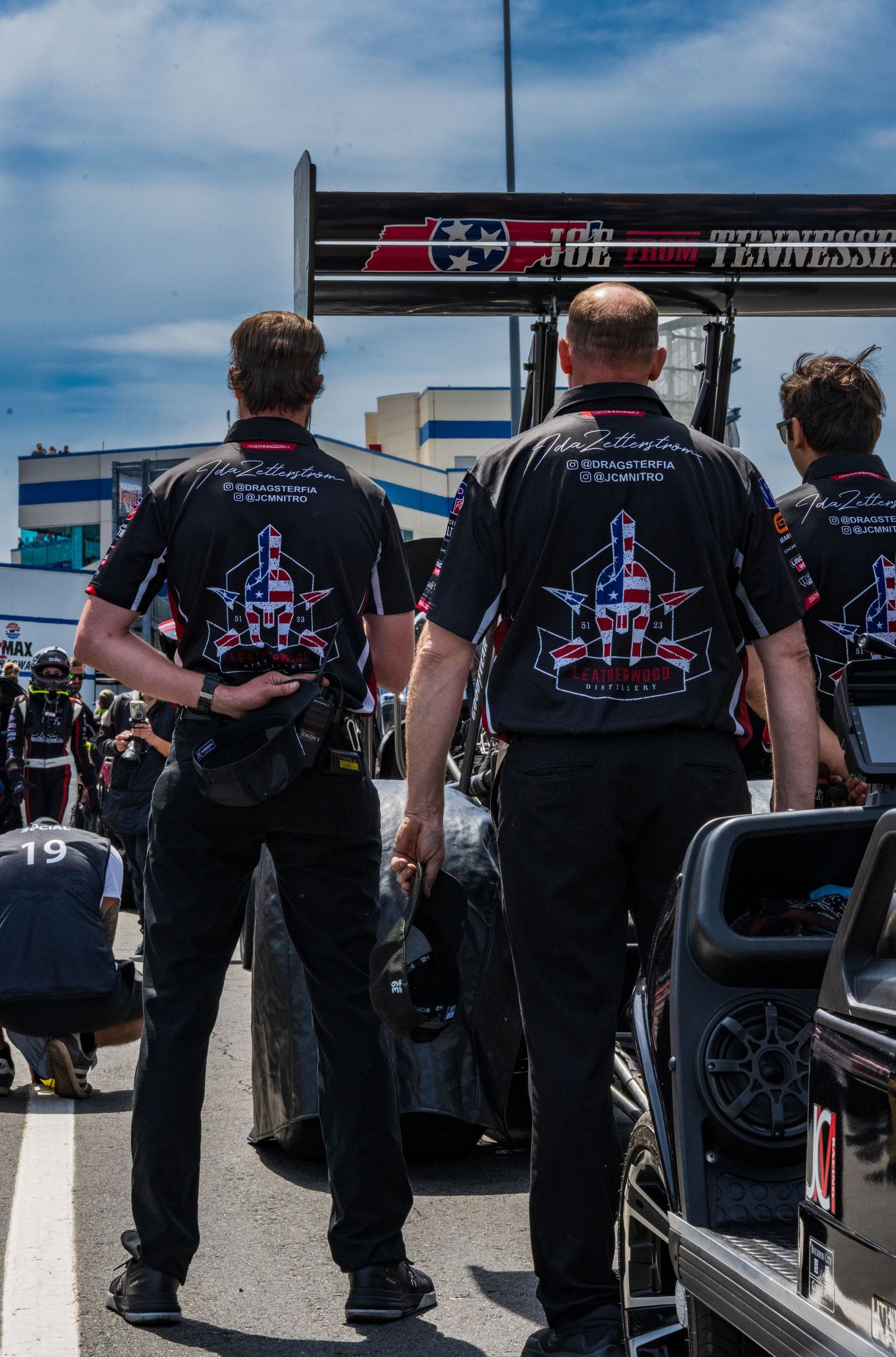 Racing team crew members in black uniforms standing together at a motorsport event.