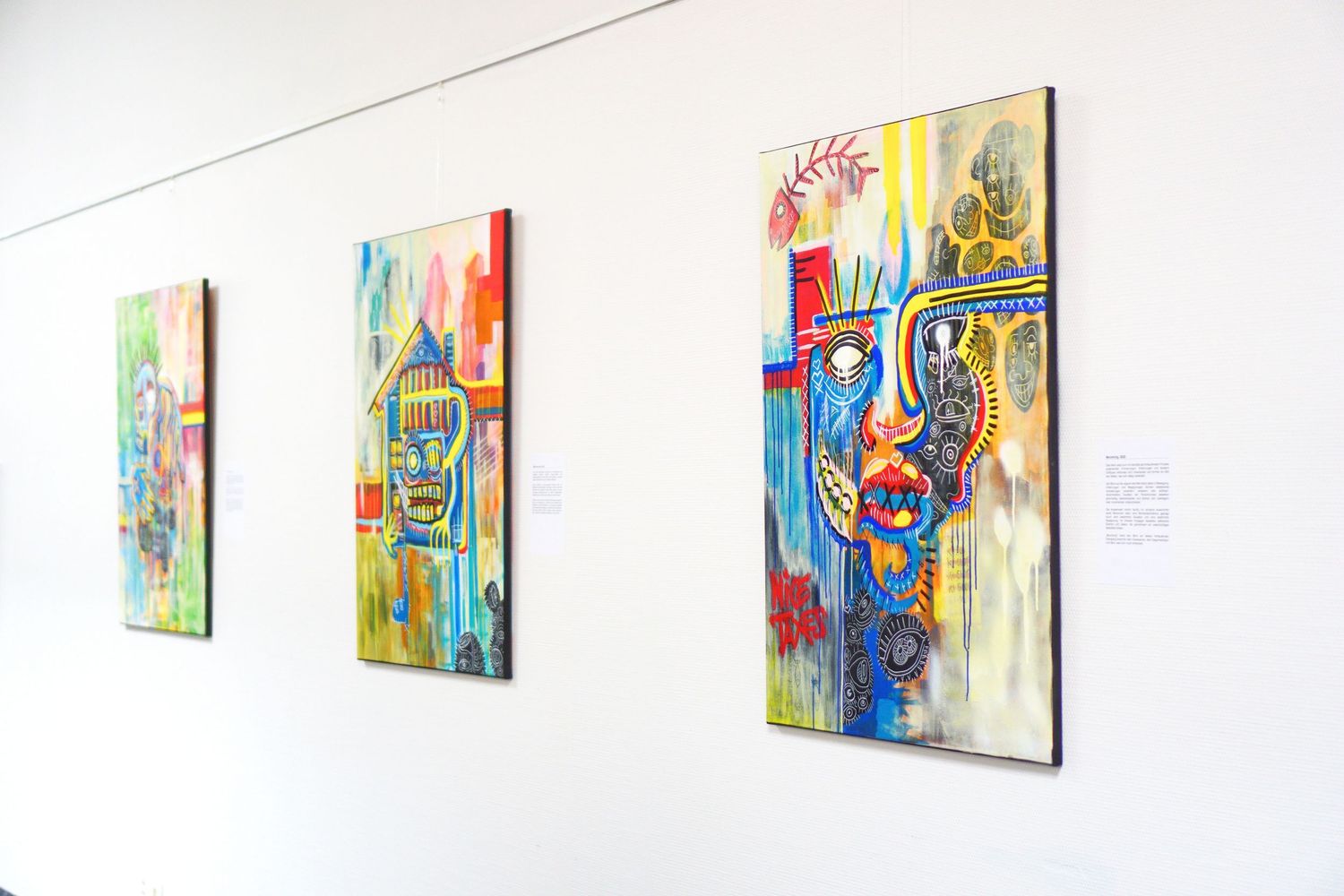 Three colorful abstract face paintings displayed on a white gallery wall in a modern art exhibition.