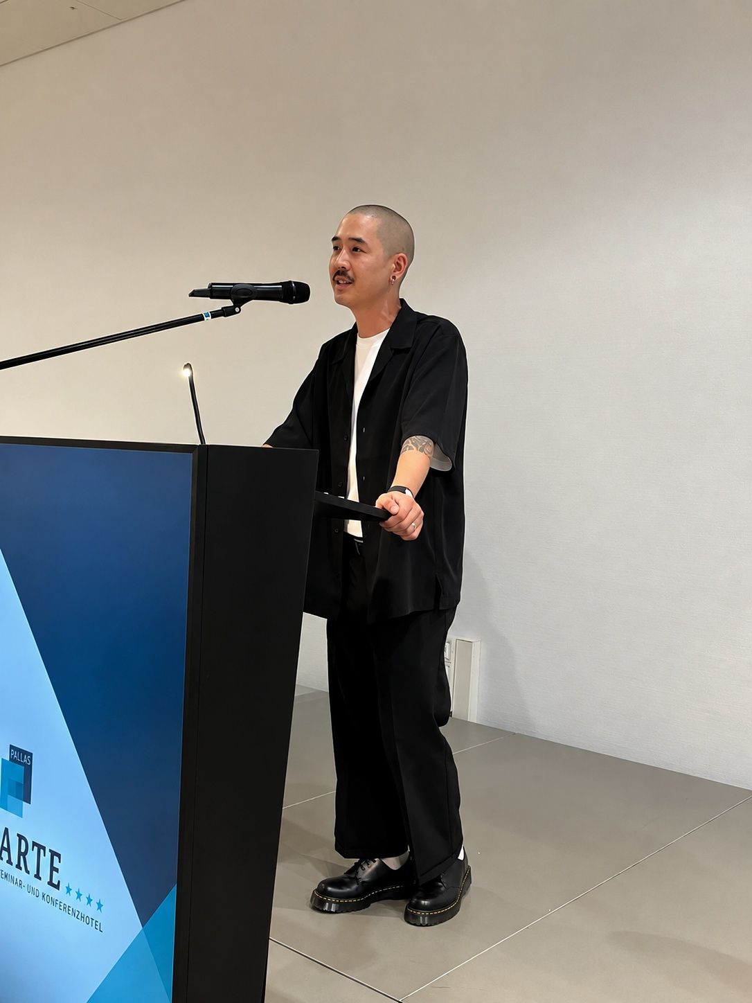 Zailou speaking at a podium with microphone at an Art event.