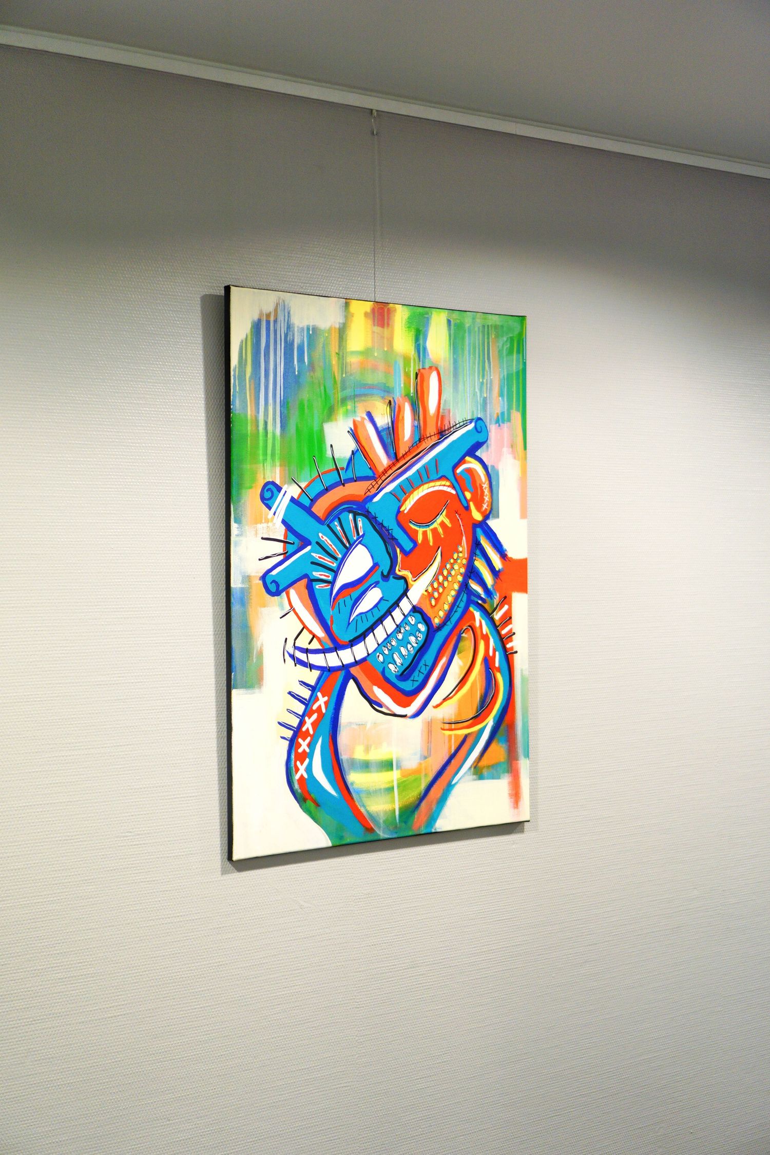 Colorful abstract painting of a heart hanging on a white gallery wall, featuring bold blue, red, and green brushstrokes.