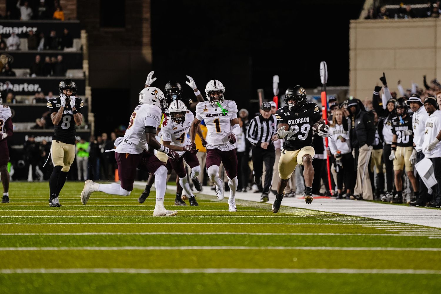 Football players run along sideline during night game action.