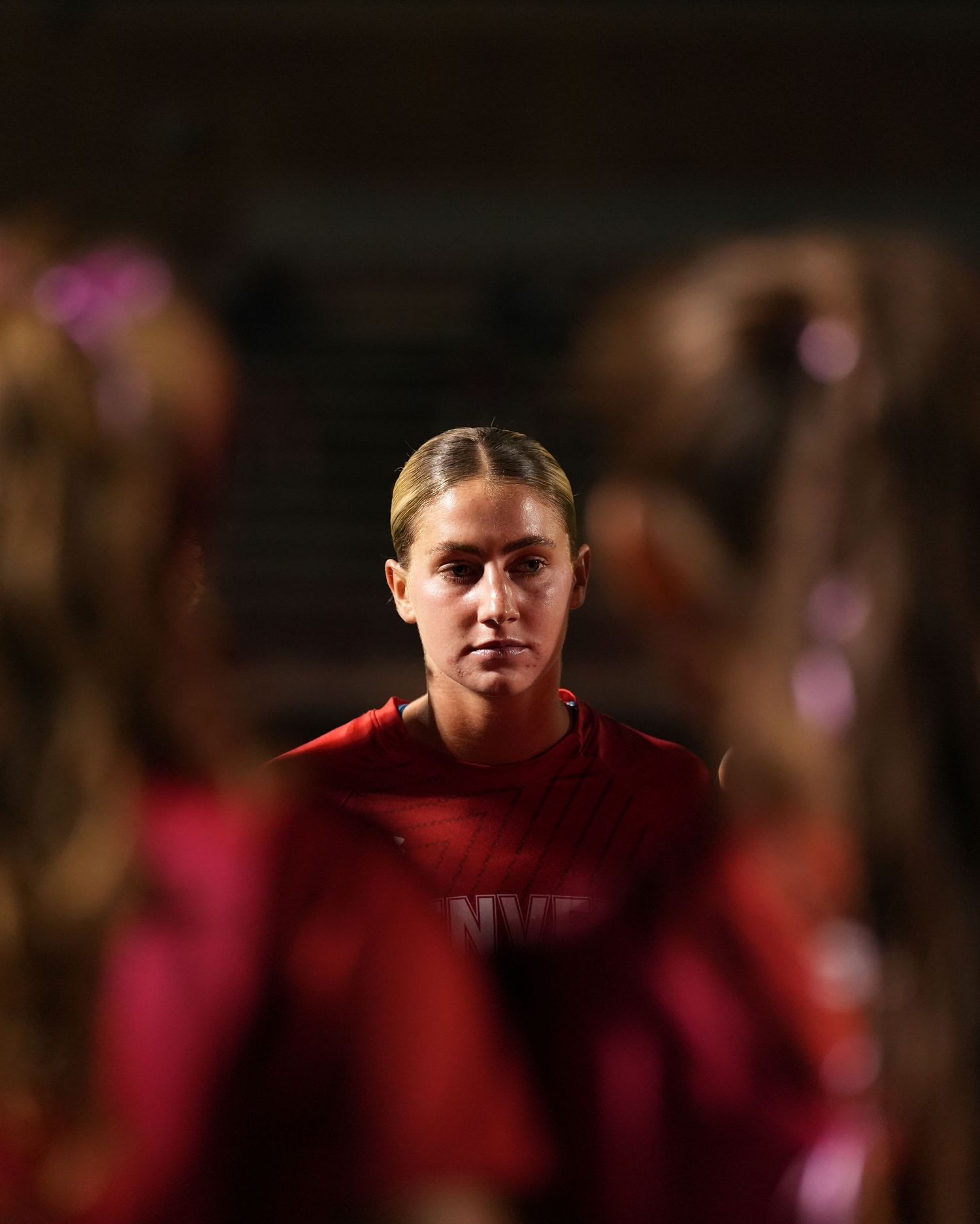 Athletes in red uniforms lined up during evening sporting event.