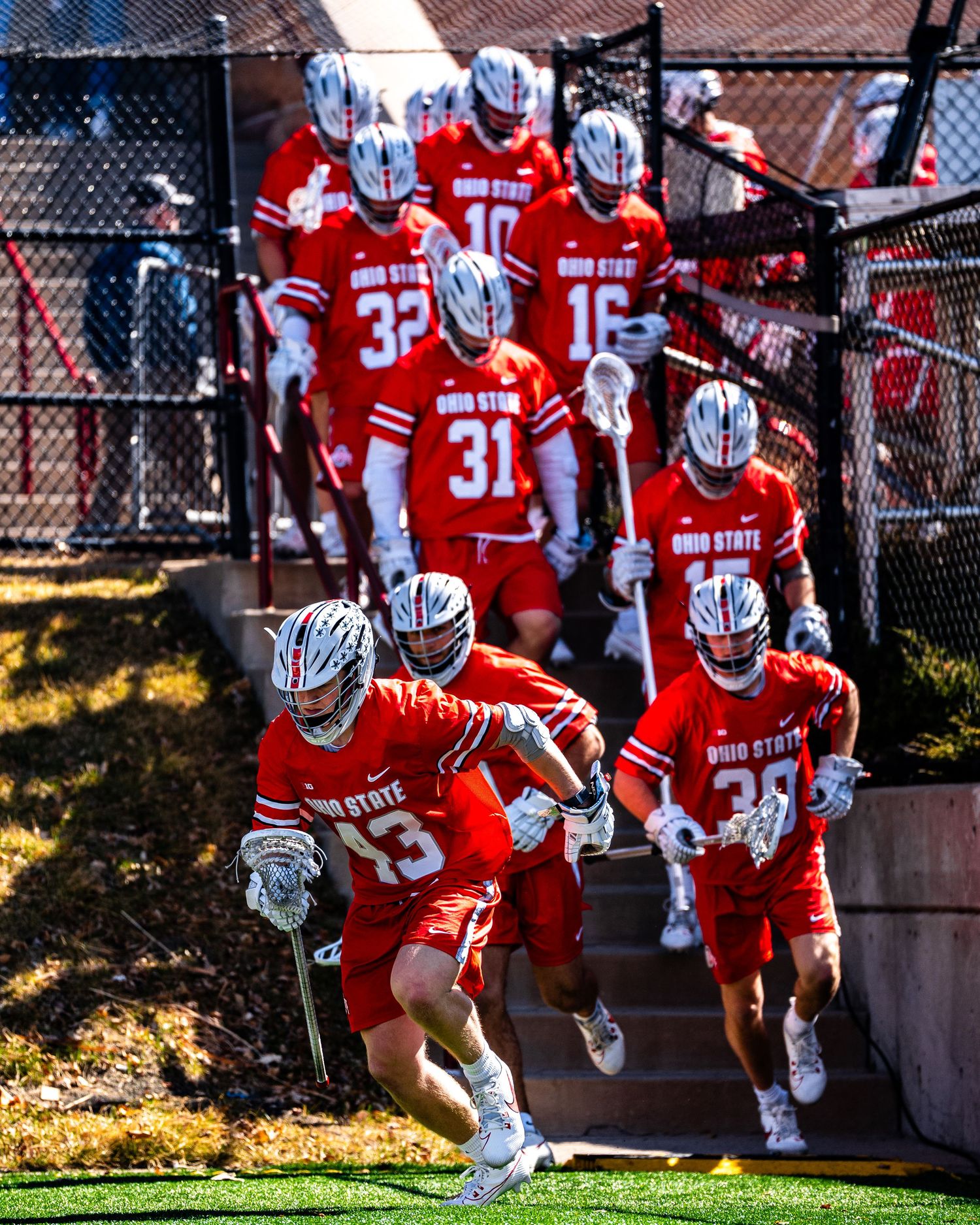 Lacrosse team in red uniforms descending stadium steps before a game.