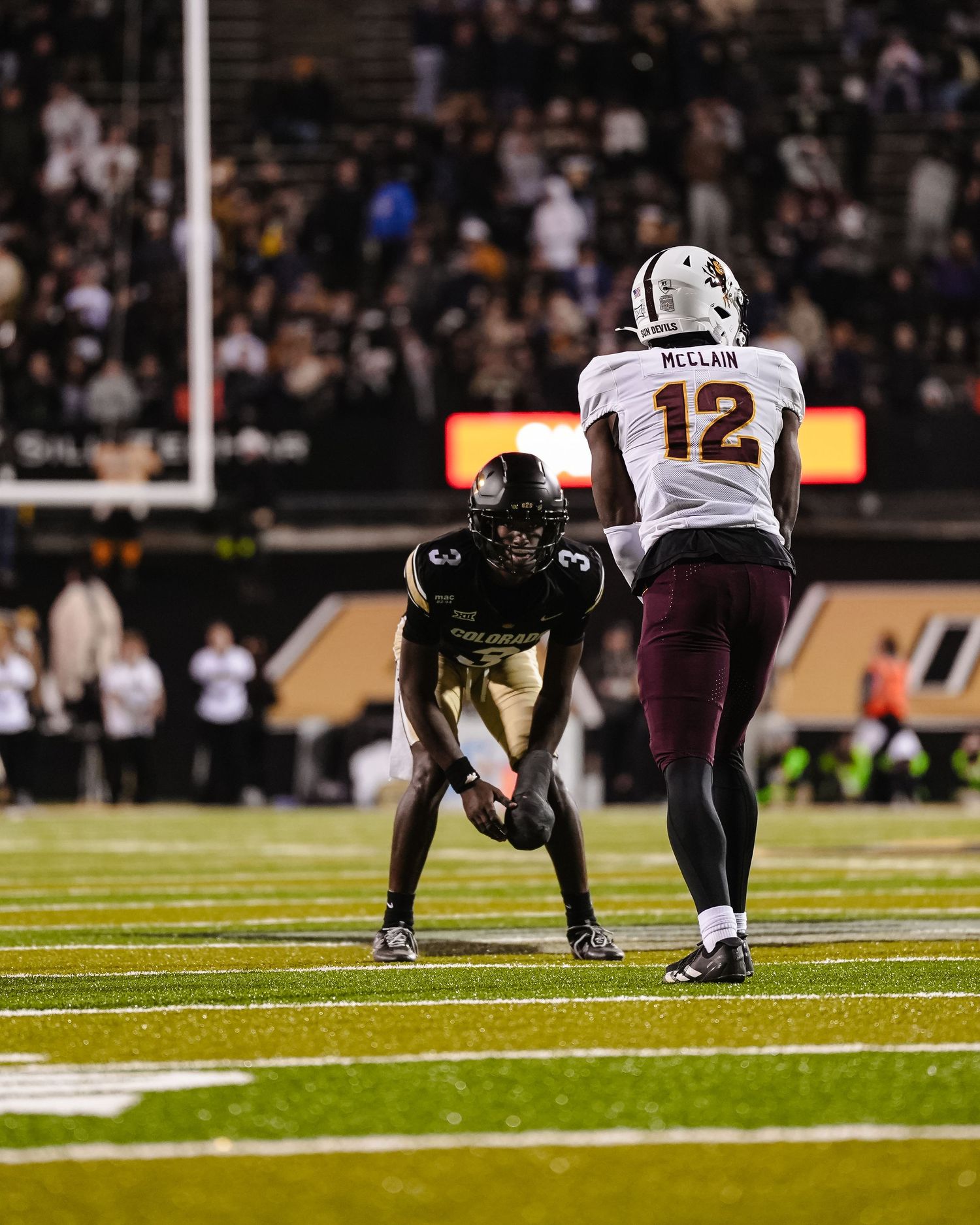 Two football players from opposing teams face off on field during game.