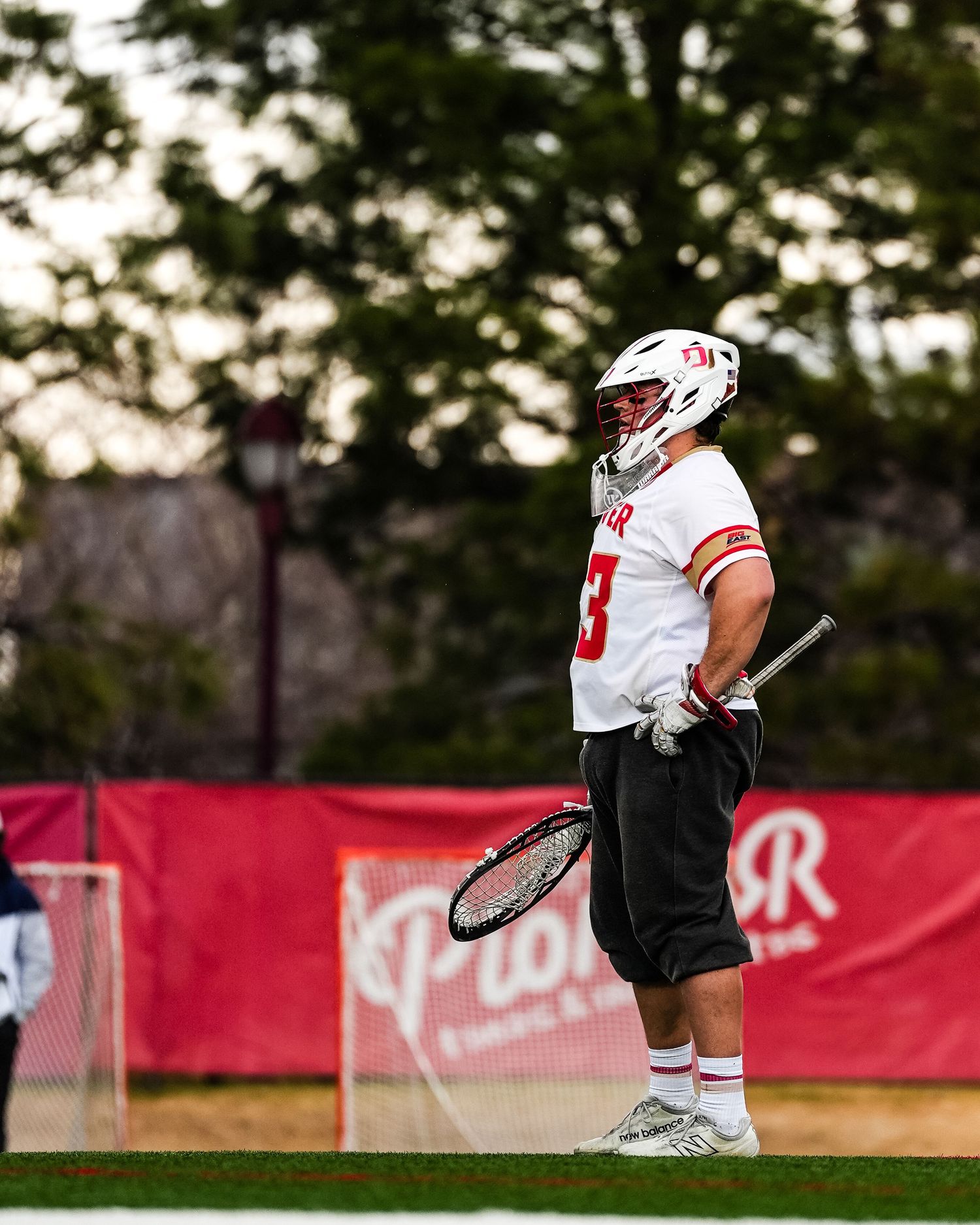 Lacrosse player in white uniform and helmet standing on field.