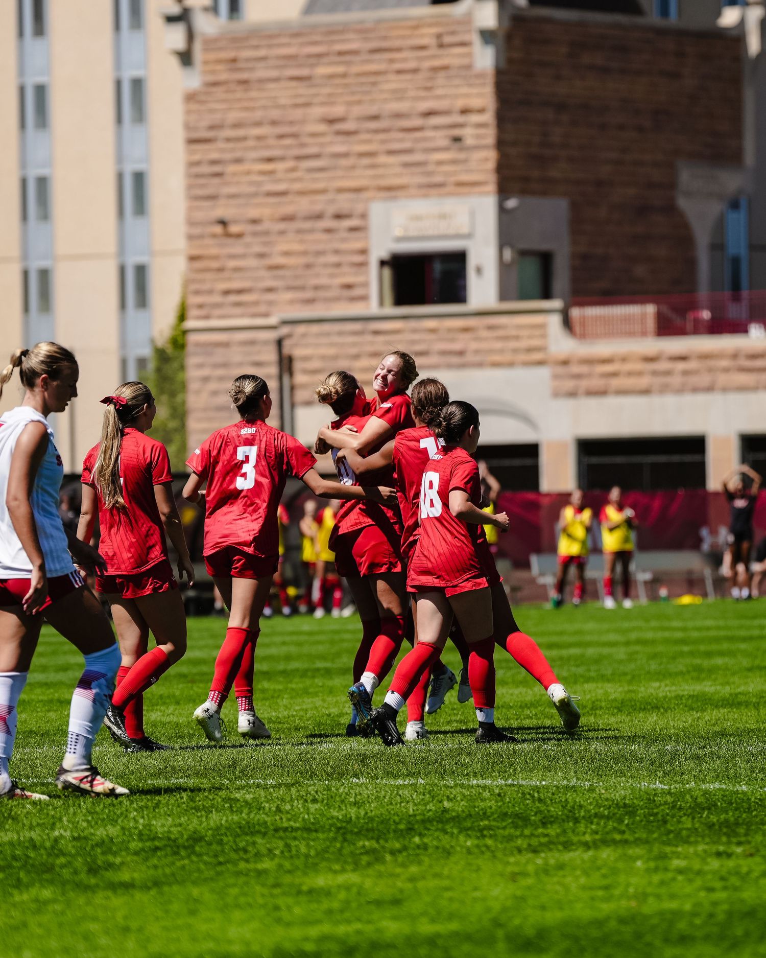 Soccer players in red and white jerseys celebrate during match on sunny field.