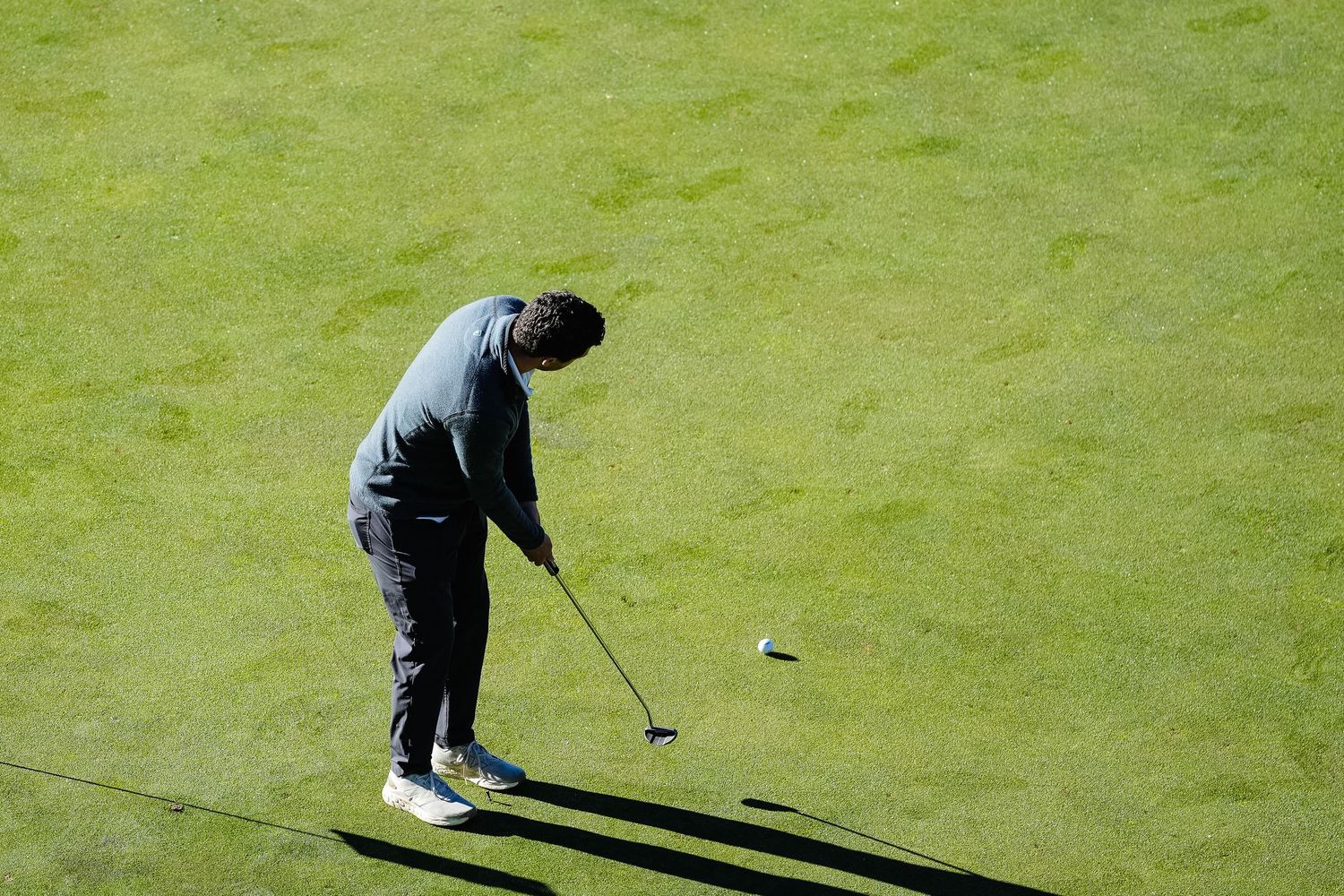 Golfer practicing putting on a bright green course under natural lighting.
