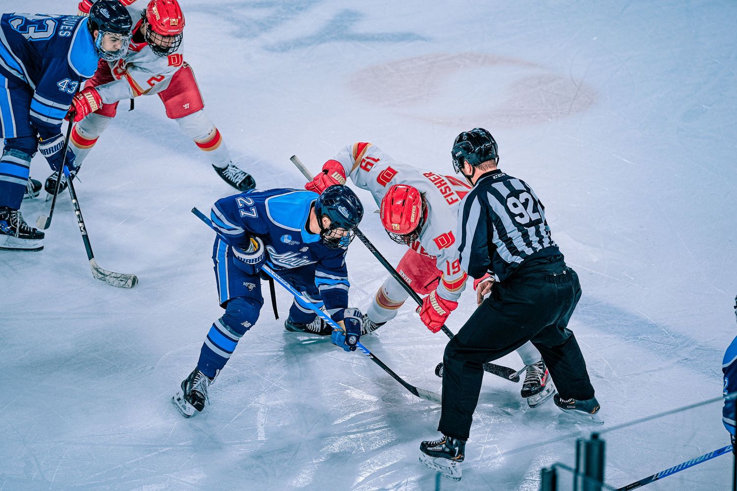 Ice hockey players in blue and red jerseys faceoff.