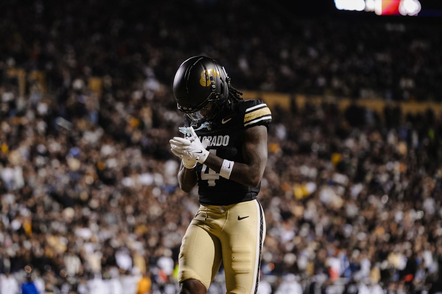 Football player in black and gold uniform celebrates during night game.