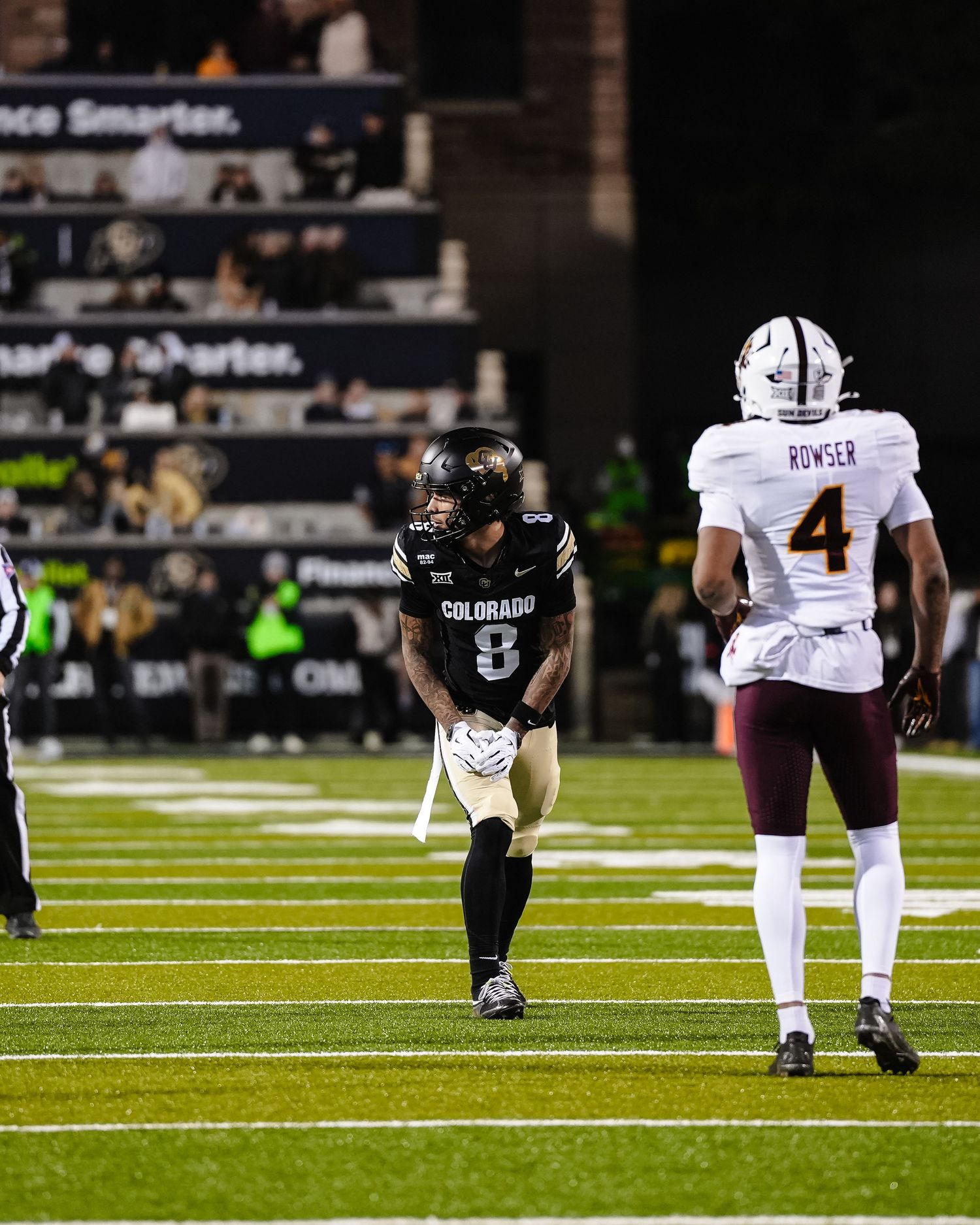 Two football players from opposing teams stand on field during game.