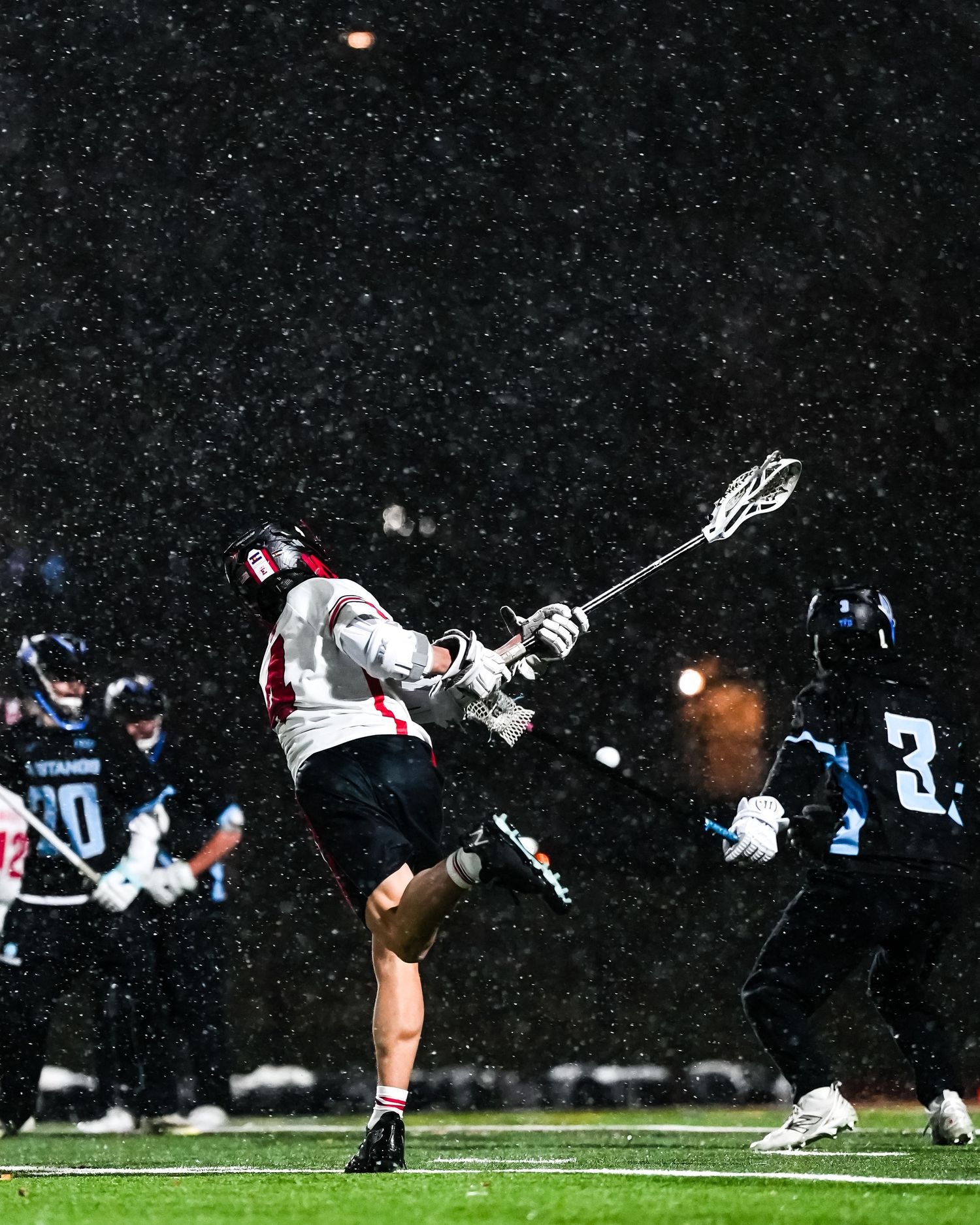 Lacrosse player shooting in the snow during a nighttime game.