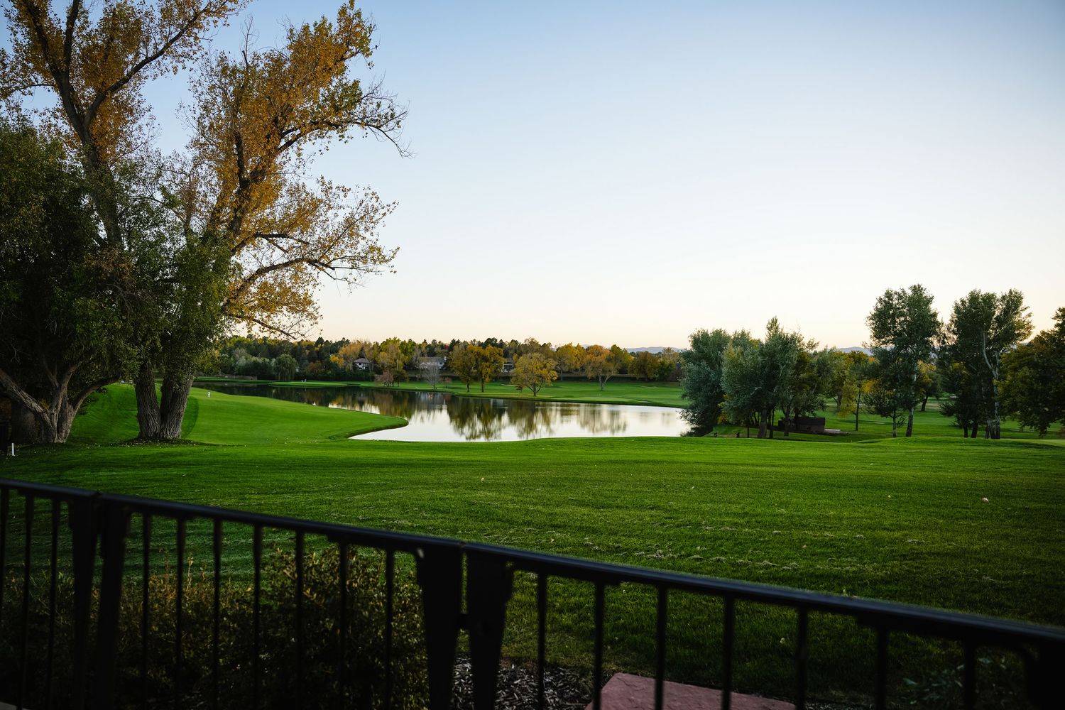 A scenic golf course landscape with a pond and trees stretching across rolling green fairways.