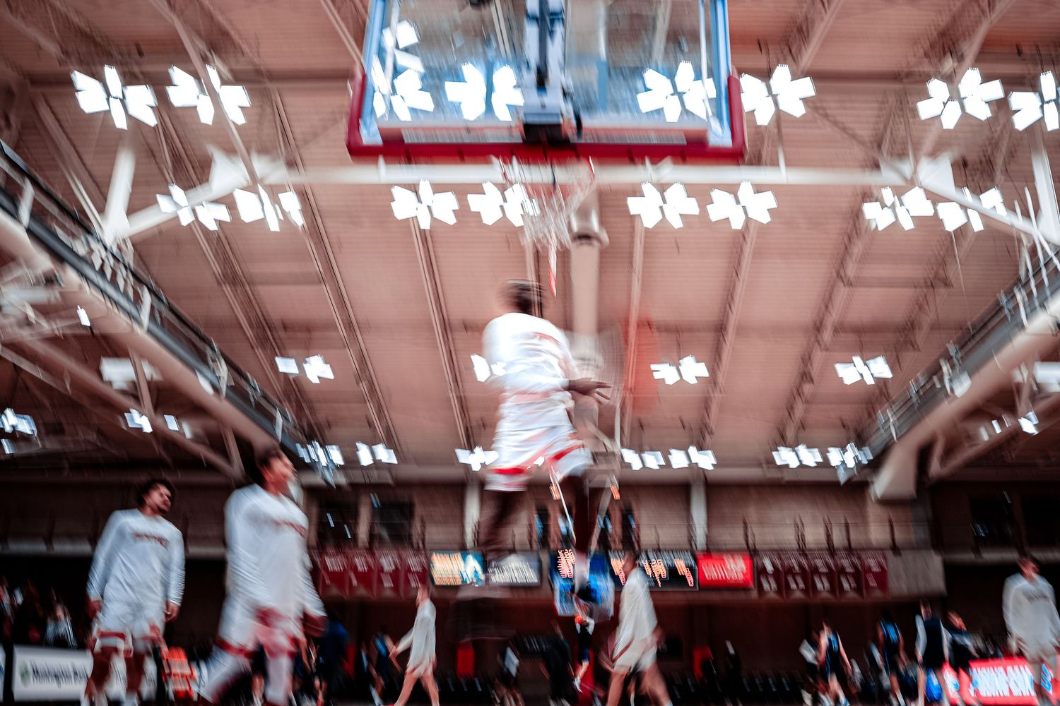 Athletes performing high-flying basketball moves during indoor game.