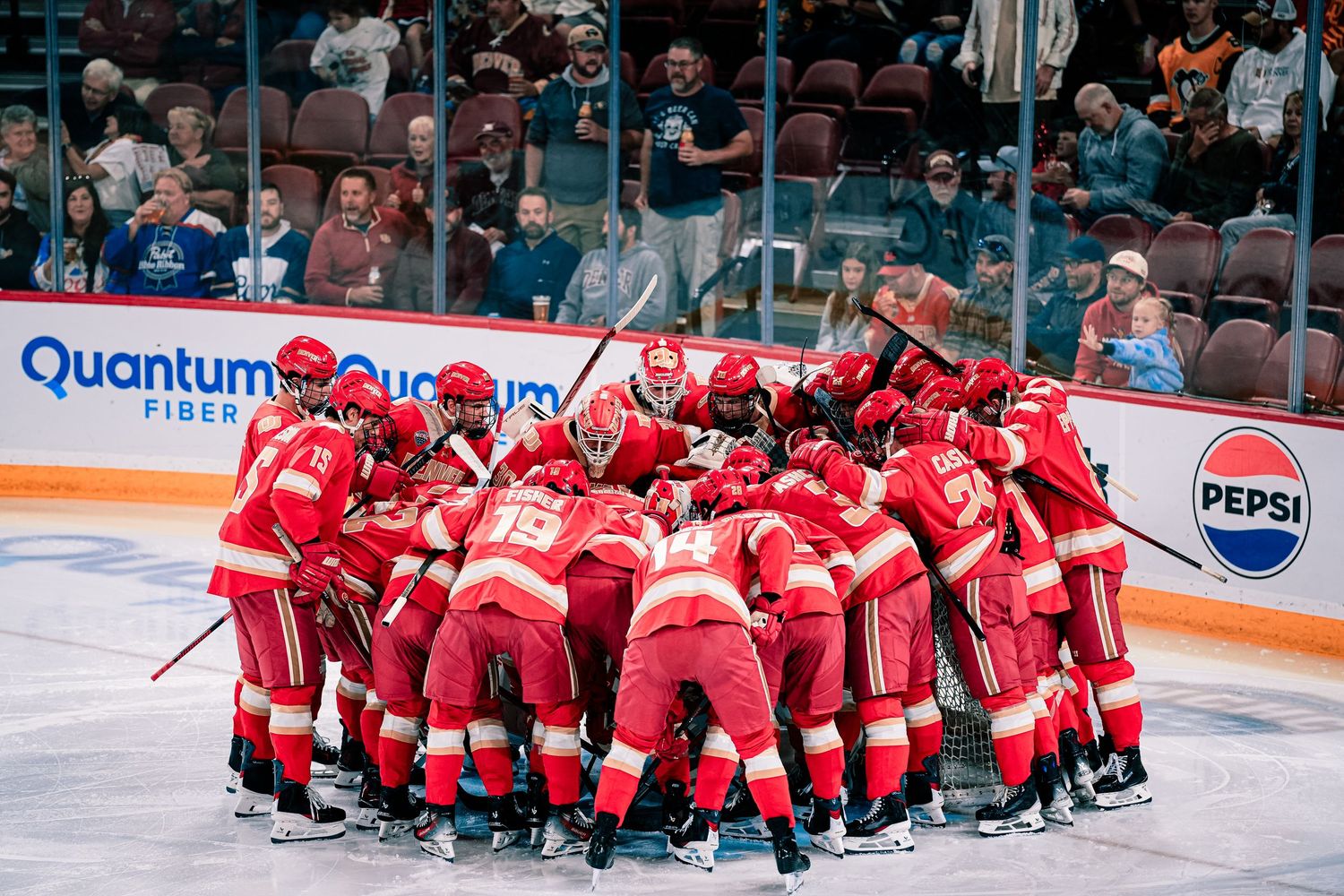 Hockey team in red uniforms huddles together on the ice before a game.