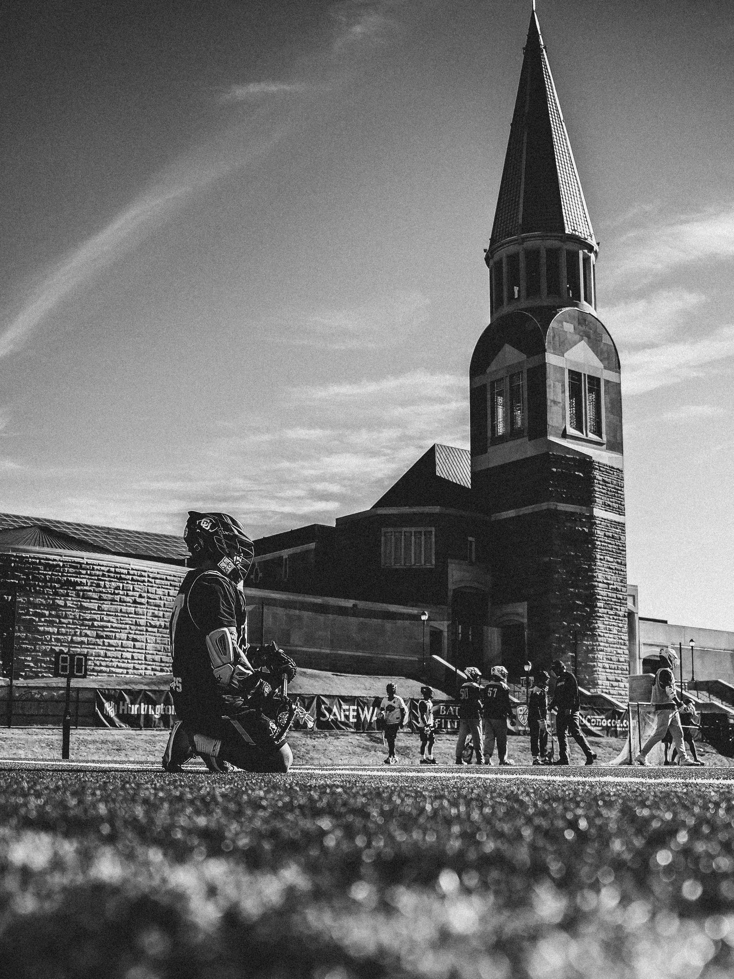 Black and white photo of lacrosse practice with bell tower in the background.