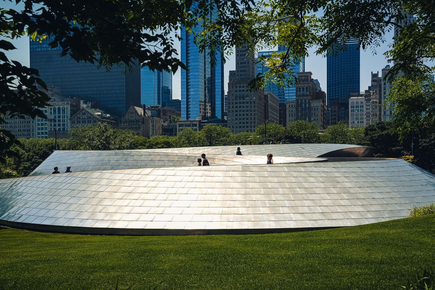 Modern curved metal structure reflects sunlight with Chicago skyline in background.