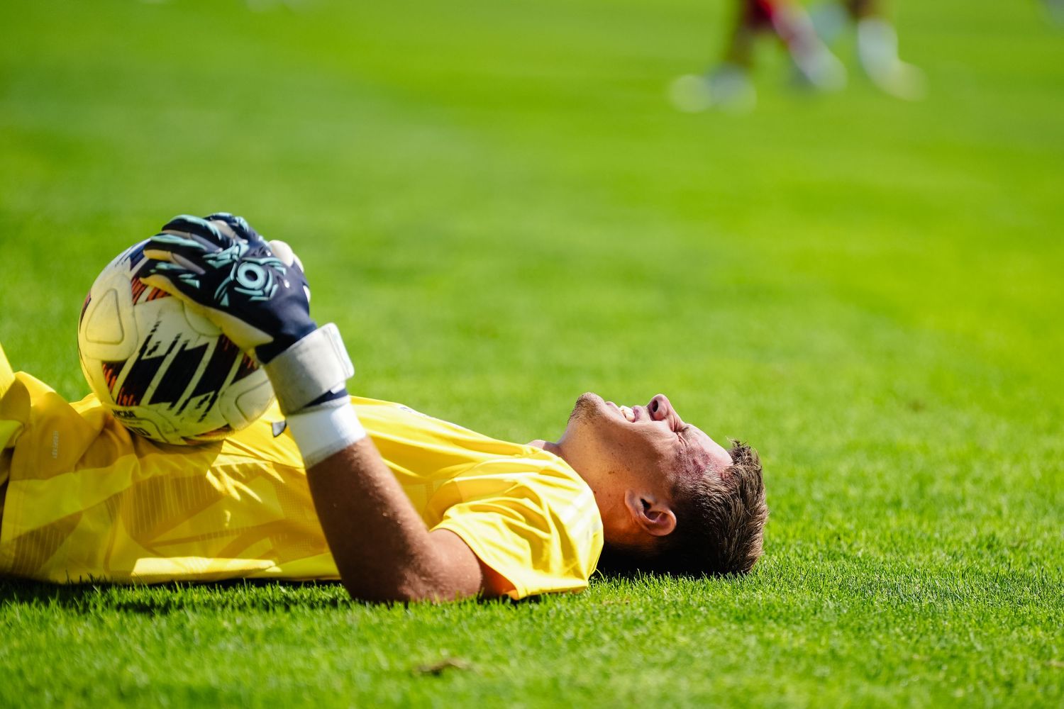 A soccer player in yellow jersey lies on green grass field during a match.