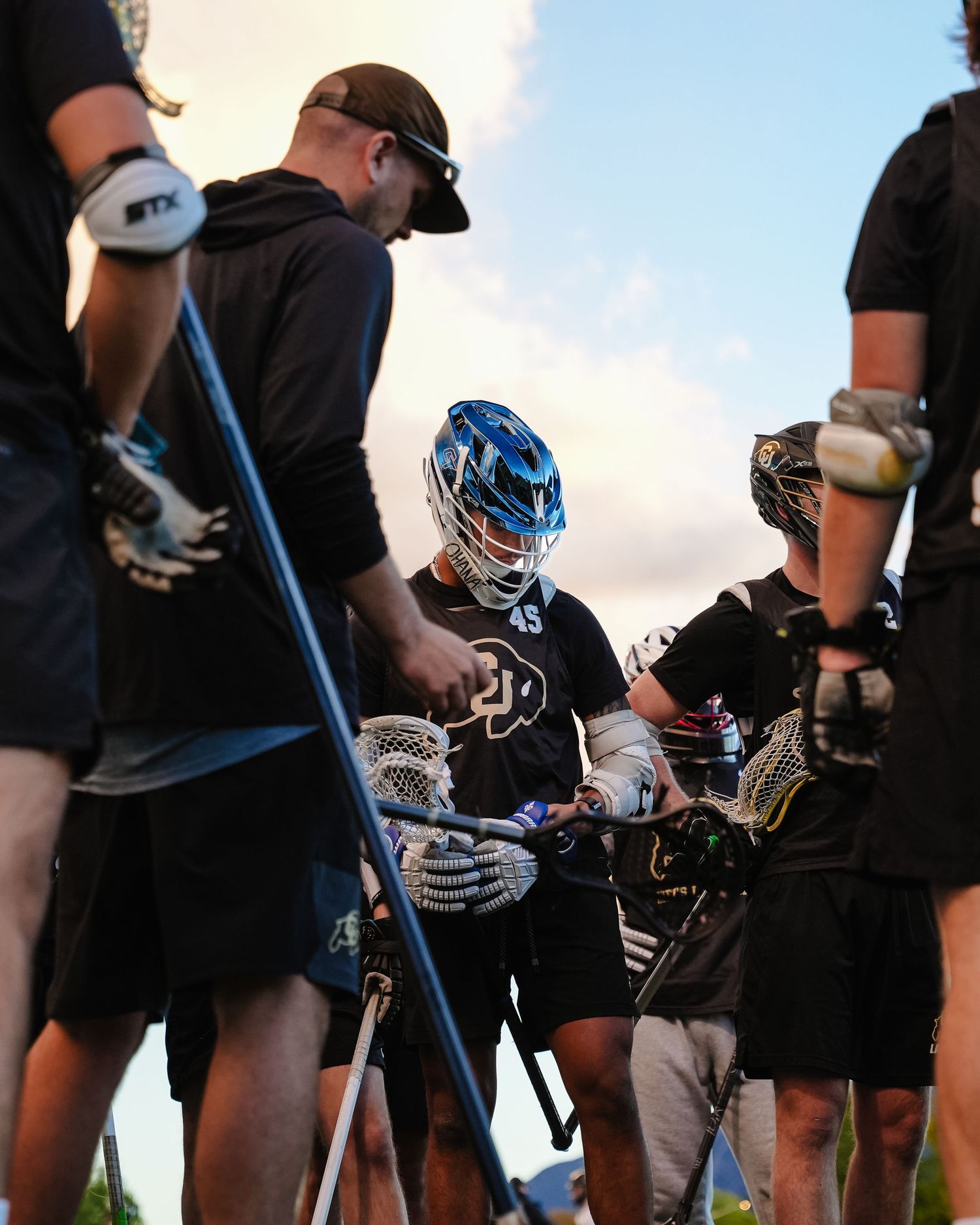 Group of lacrosse players holding sticks during evening practice session.