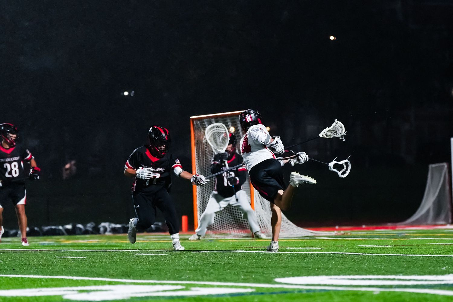 Night game action on lacrosse field with players in motion.
