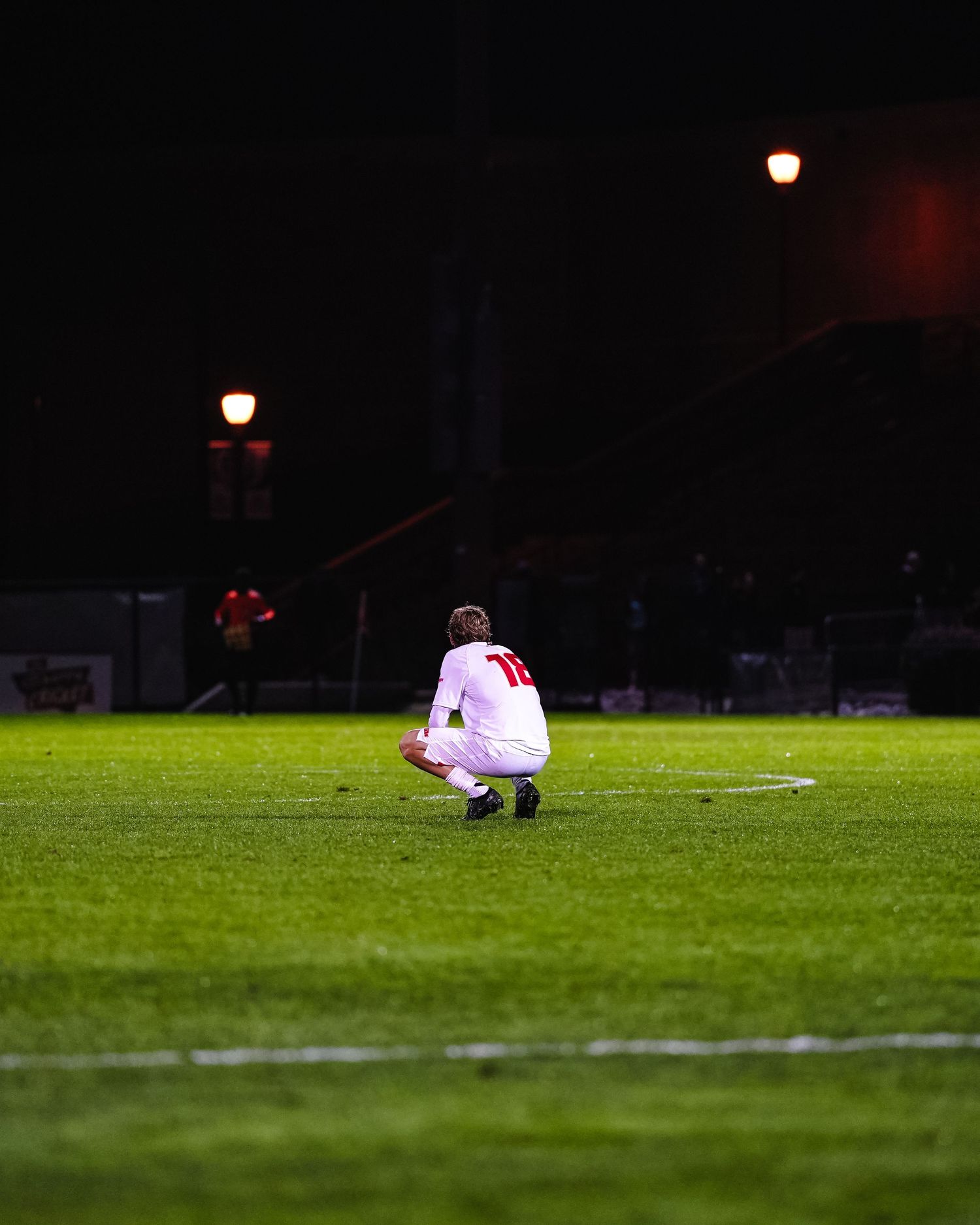 Player in white uniform lying on illuminated soccer field at night.