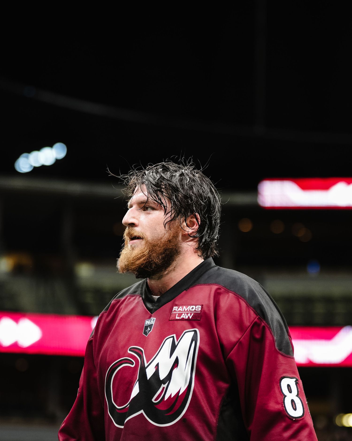Professional lacrosse player in maroon jersey celebrating during indoor game.