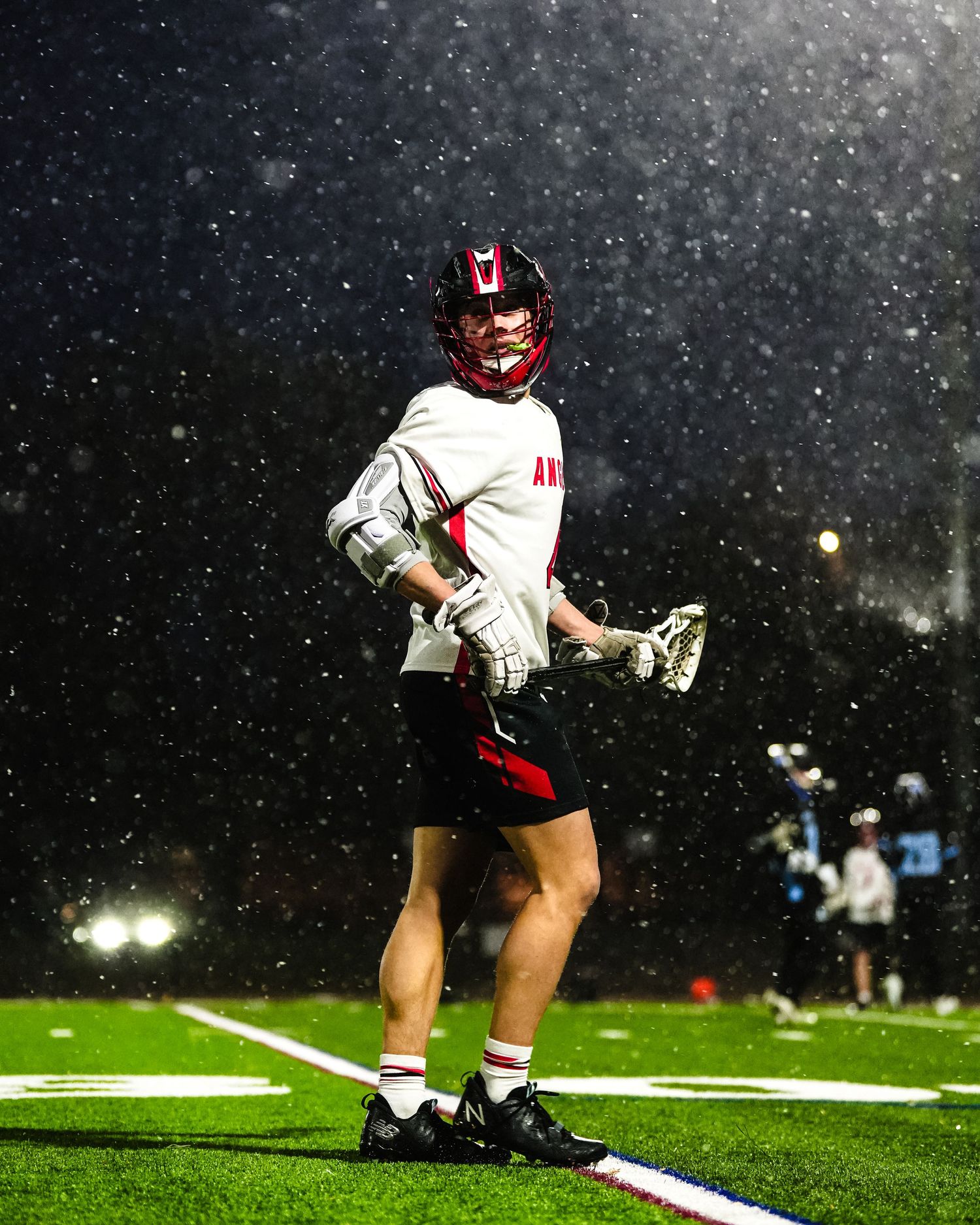 Lacrosse player competes on snowy field during nighttime match.