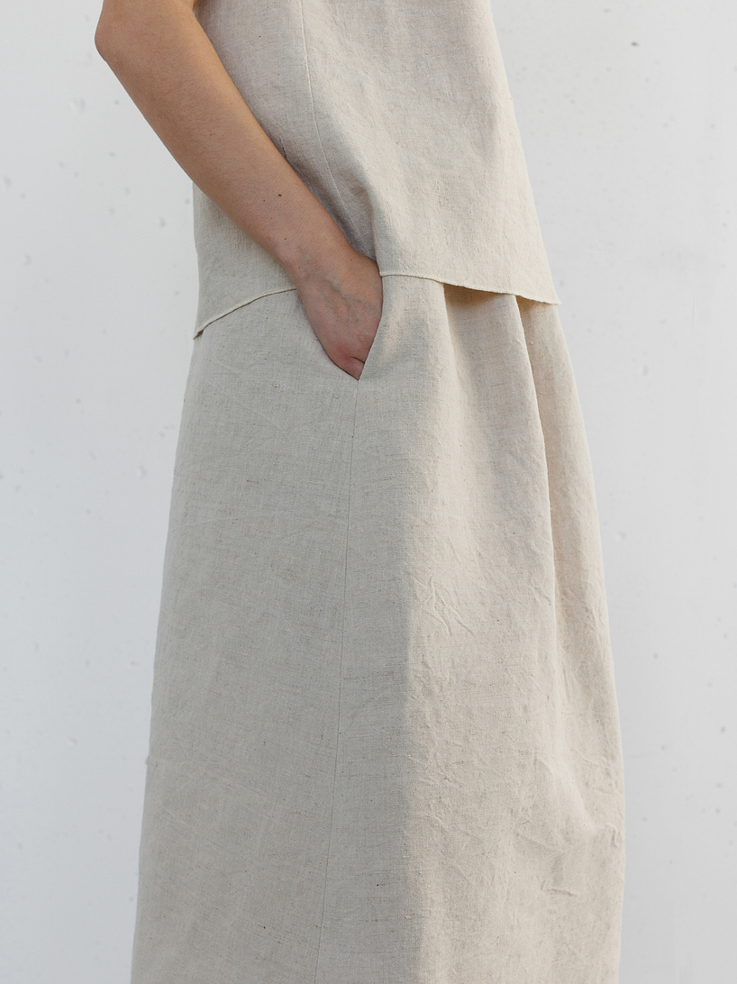 Close-up of a model wearing a natural linen midi skirt and matching top with hand in pocket.