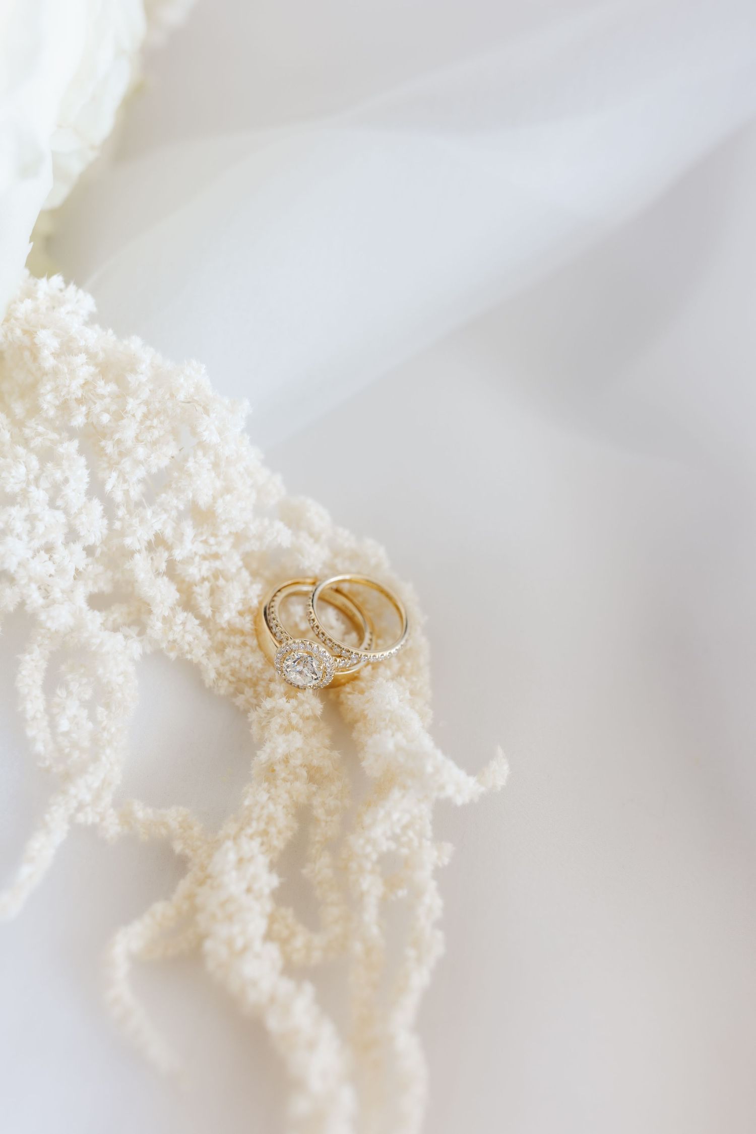 Two gold wedding bands resting on twisted ivory seed pearl necklace on soft white tulle fabric.