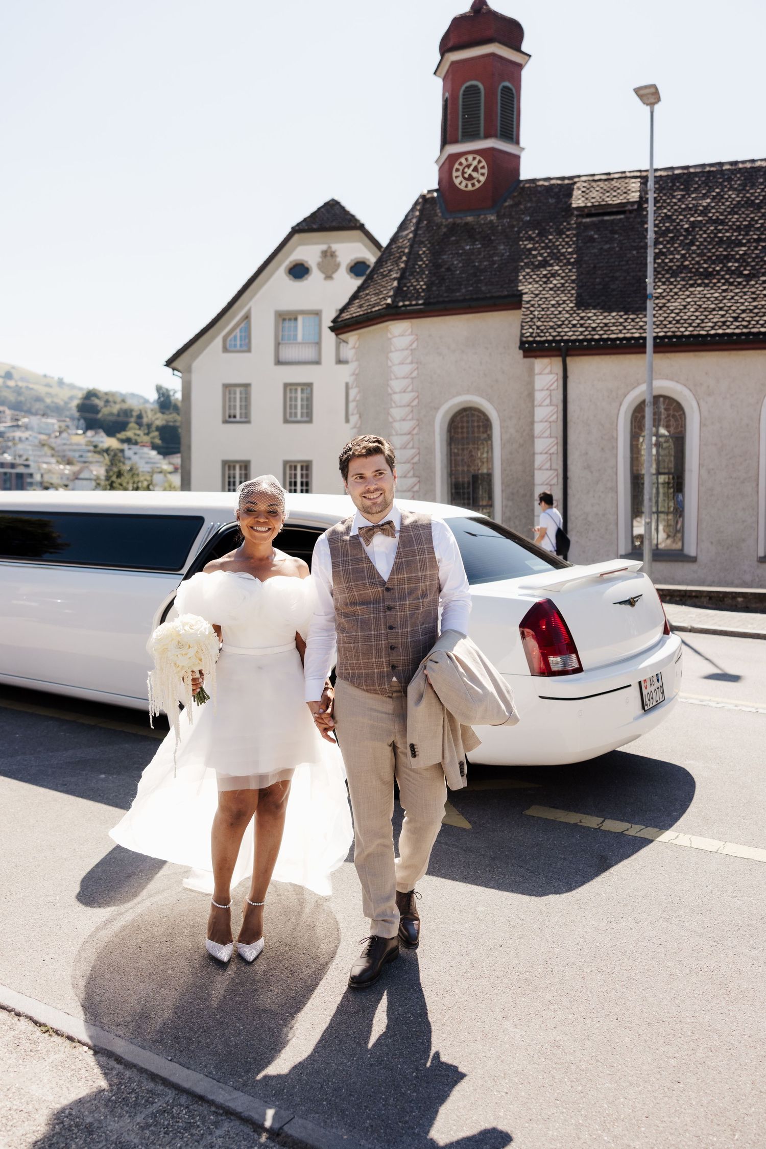 Interracial newlywed couple posing in front of a white limousine and church on their wedding day.