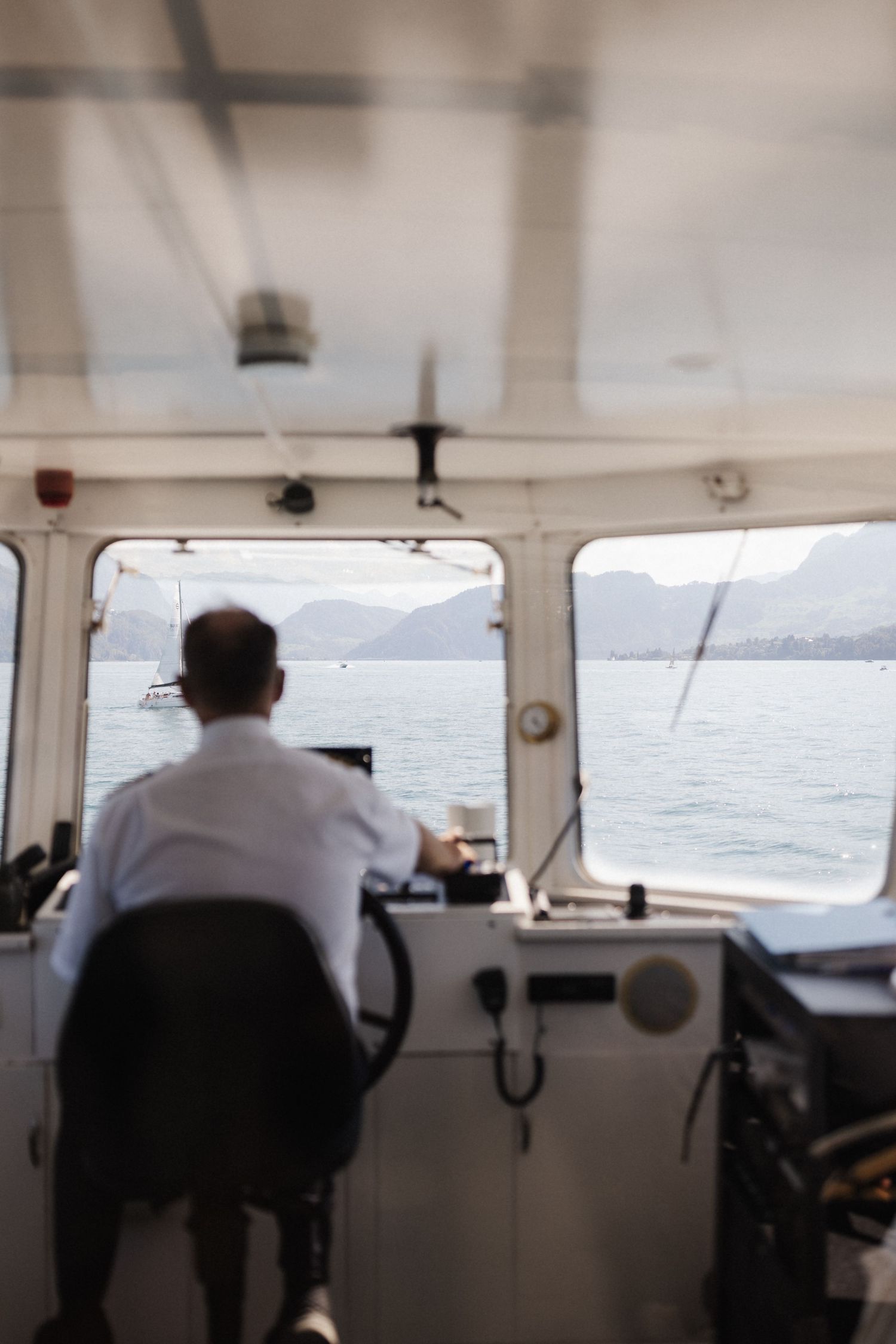 Boat captain seated at helm navigating calm blue waters with mountain views through the windshield.
