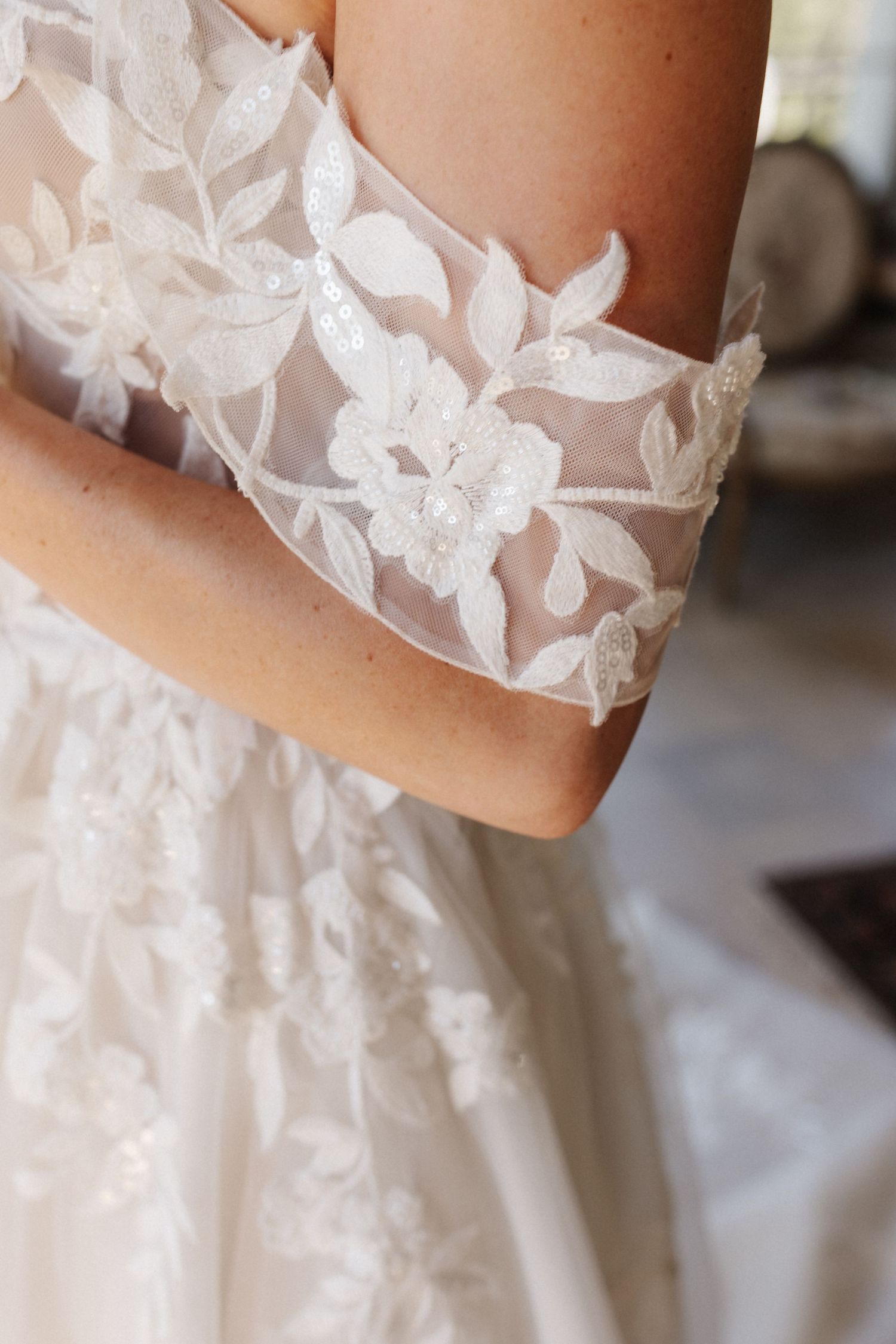 Detail shot of an off-shoulder wedding dress sleeve with intricate floral lace and pearl embellishments.