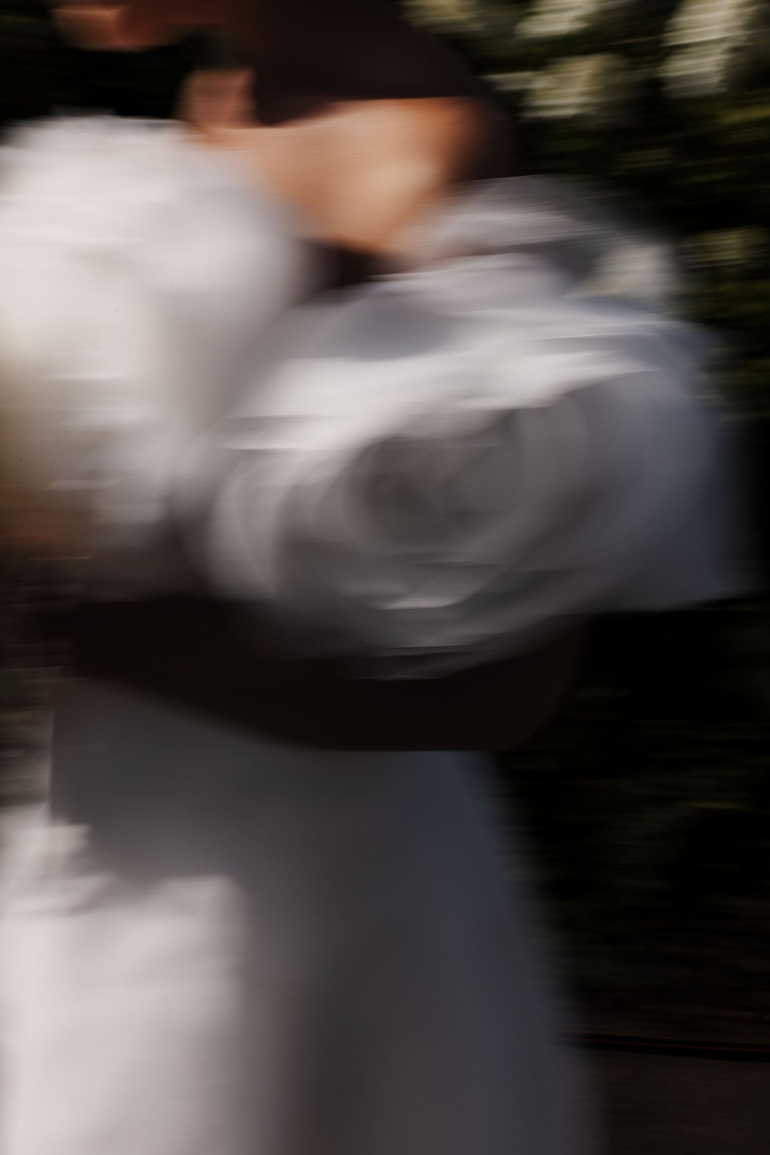 Artistic blurred motion photo of bride in white wedding dress holding bouquet outdoors.