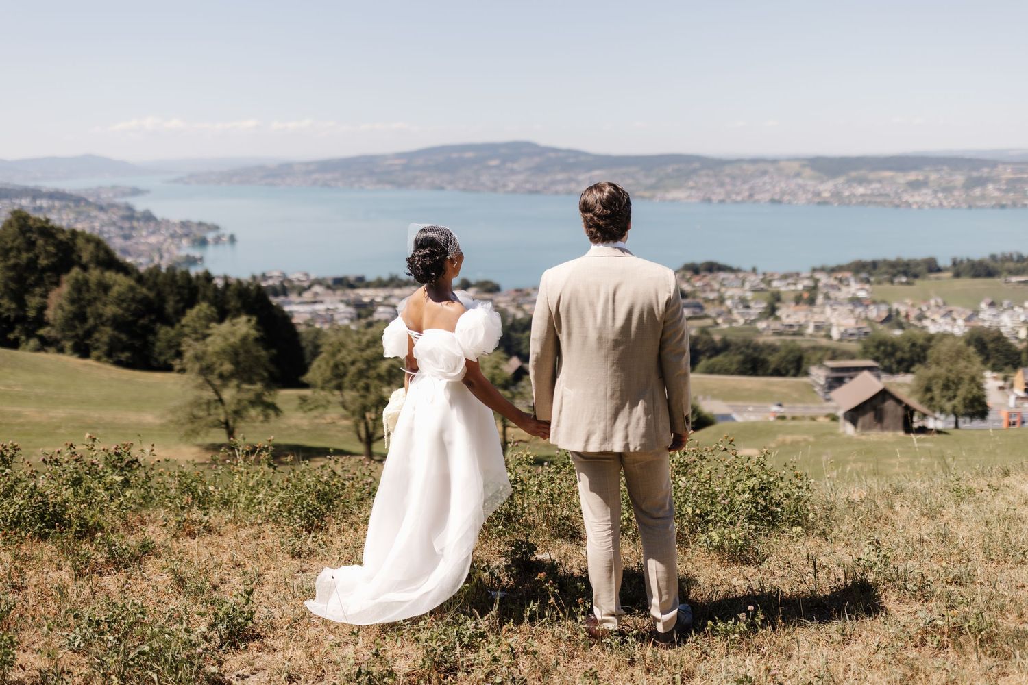 Bride and groom holding hands overlooking a scenic lake and city view on their wedding day.