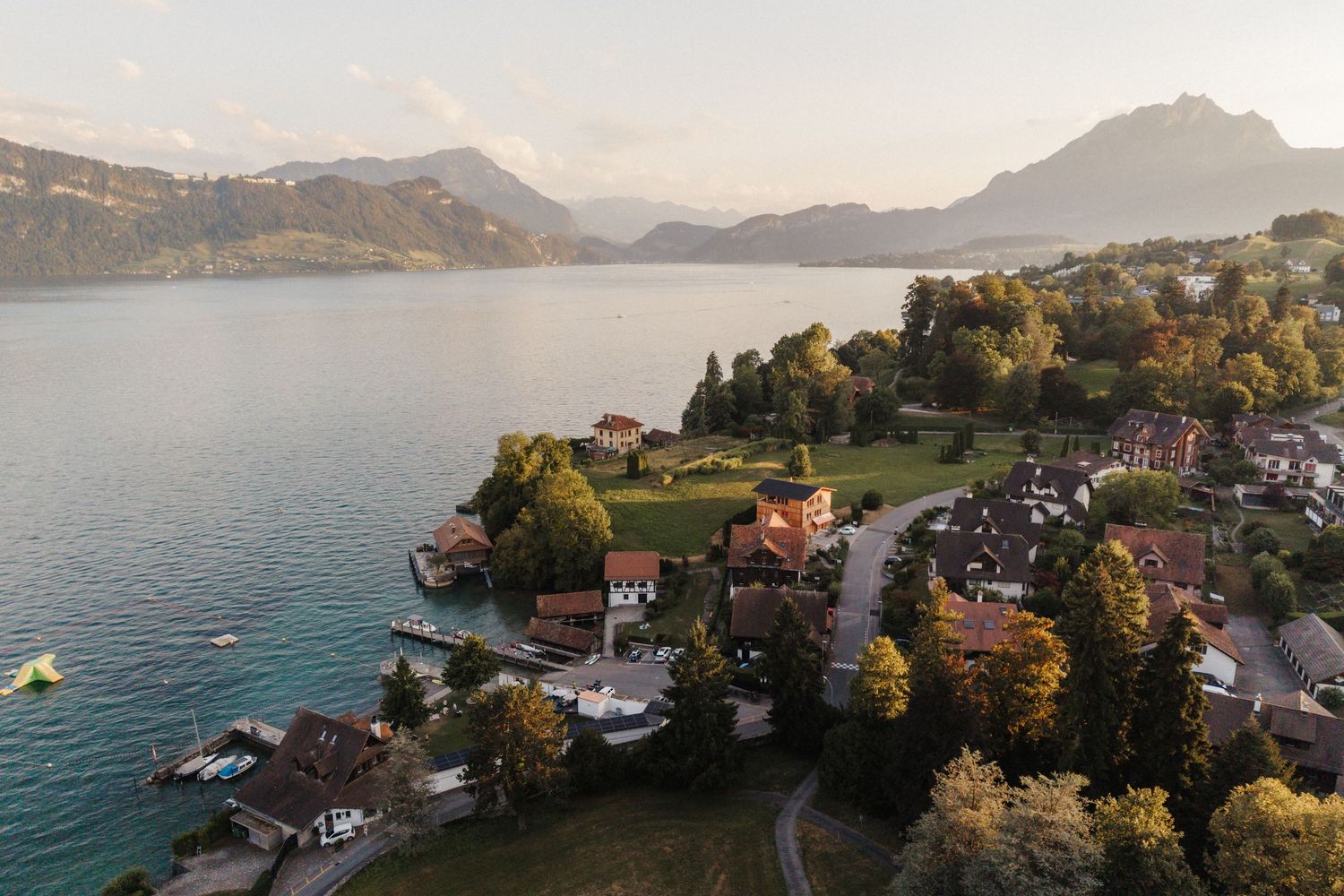 Aerial view of a charming lakeside village with colorful autumn trees along the turquoise alpine lake shore.