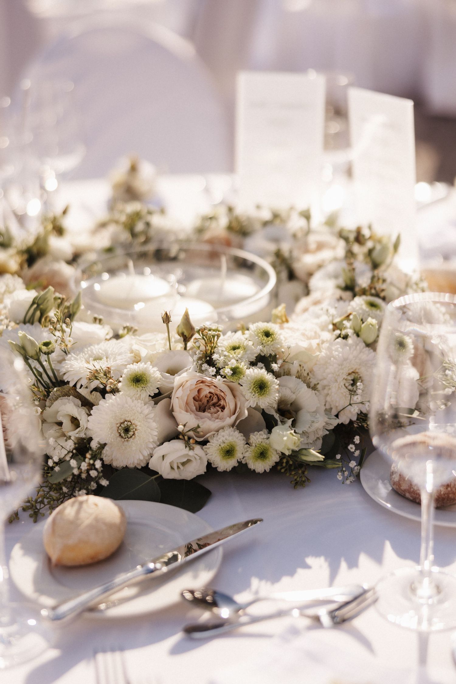 A circular floral centerpiece of white chrysanthemums and pink roses surrounds floating candles on a wedding table.