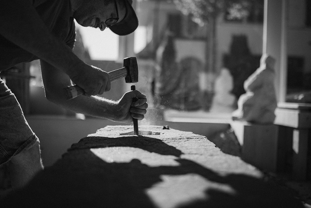 Artist carving stone with hammer and chisel in a sculptor's workshop in black and white.