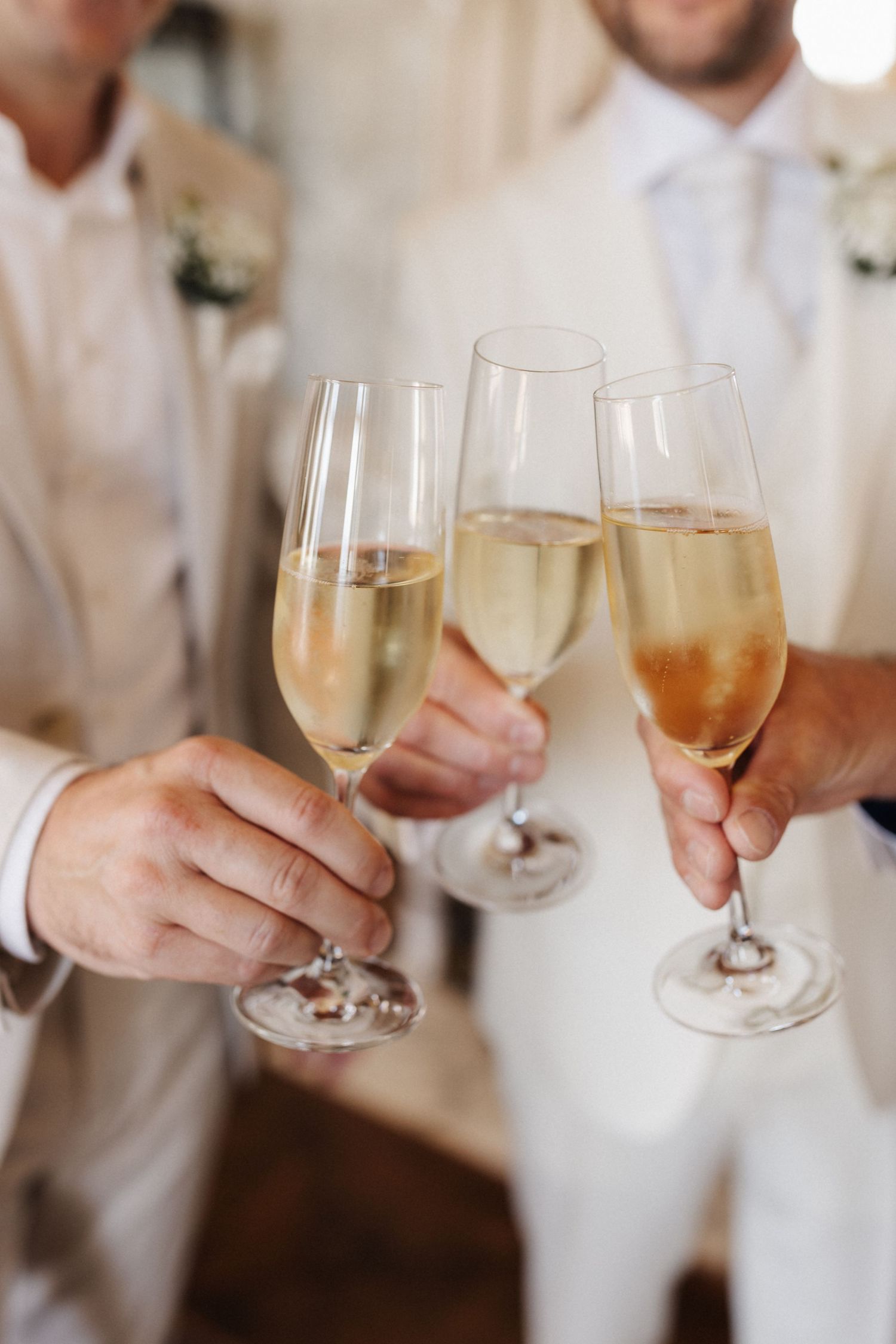 Close-up of three champagne glasses clinking in celebratory toast at wedding preparation.