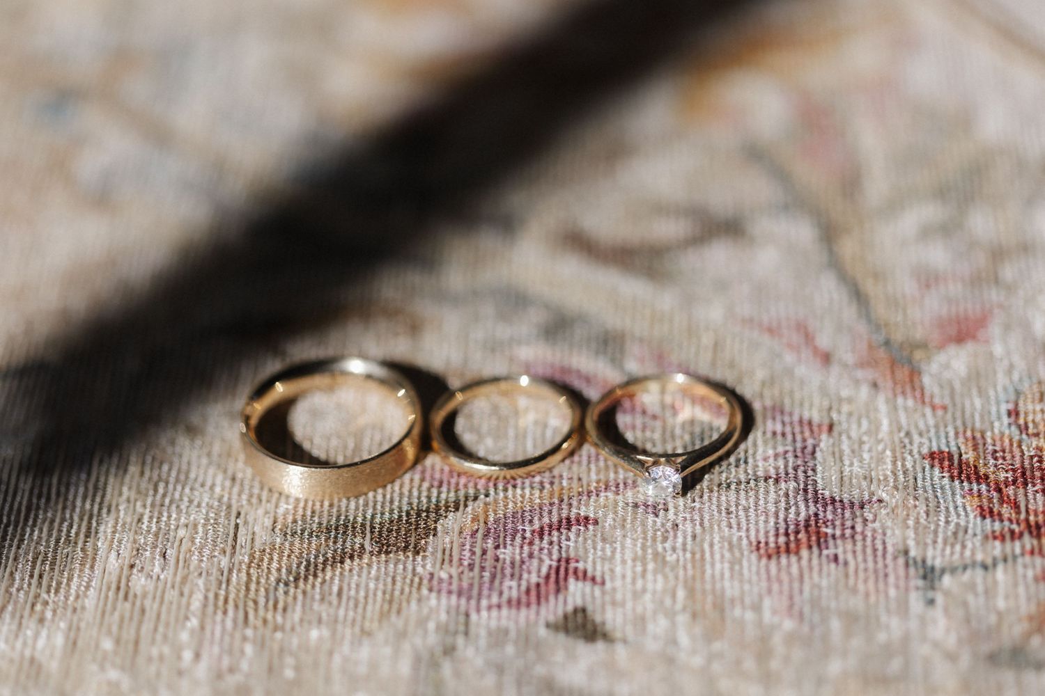 Three gold wedding and engagement rings arranged on a floral vintage rug.