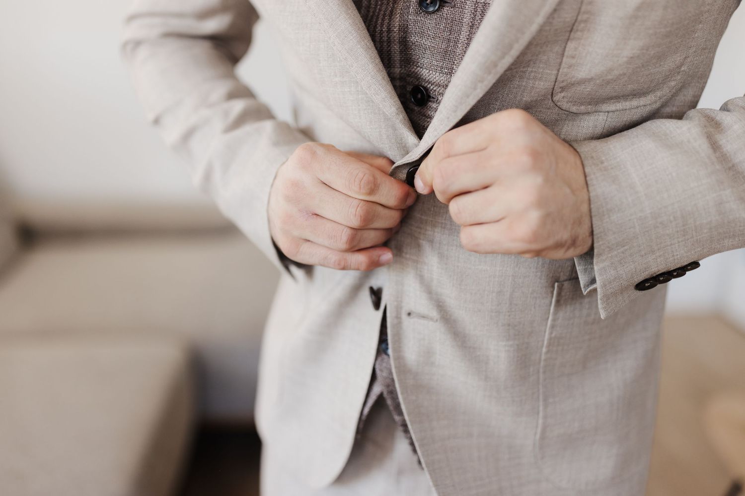 Close-up of a man buttoning a light beige suit jacket over a patterned vest.