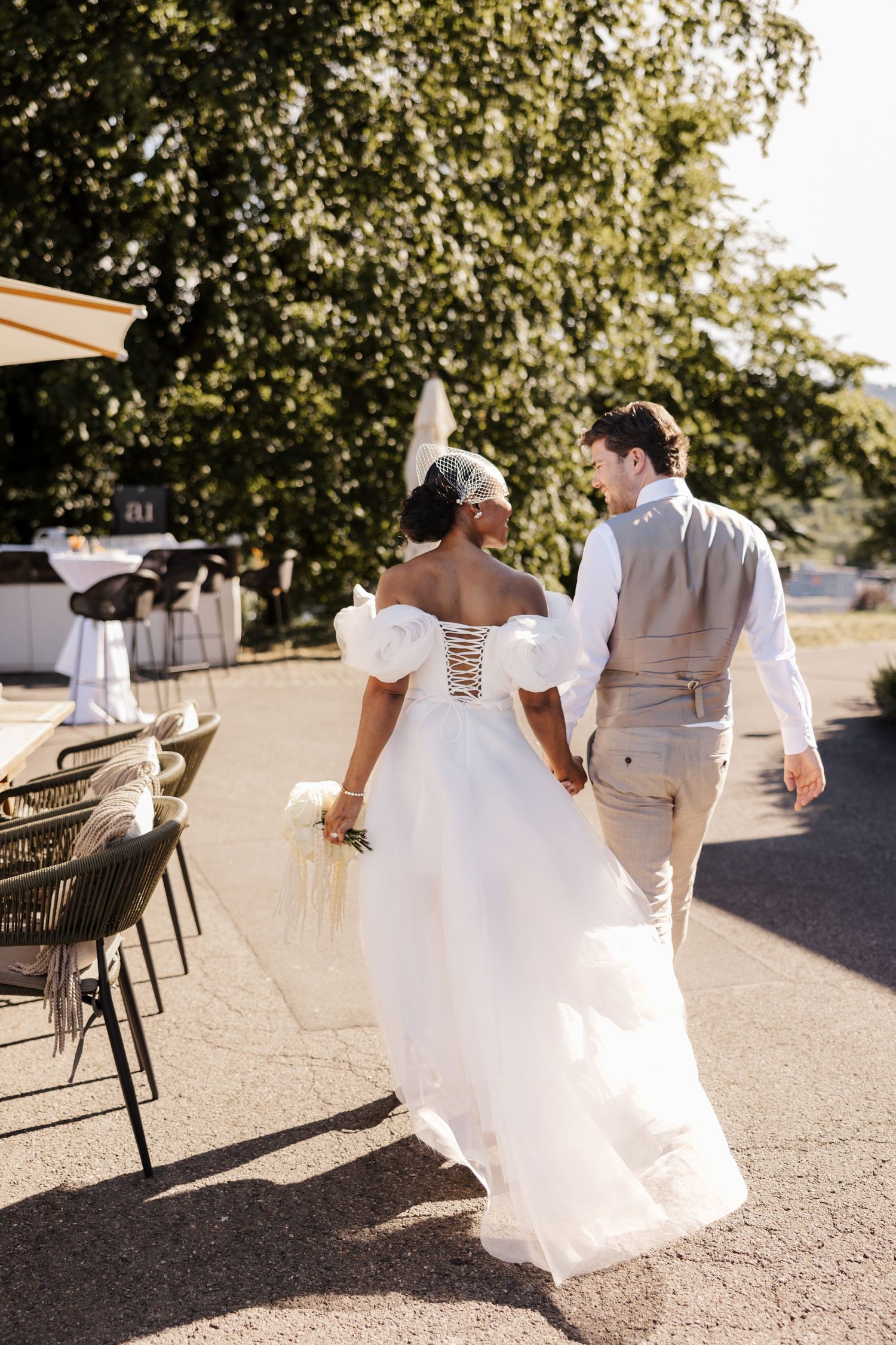 Bride and groom walking hand in hand outdoors, bride wearing a white ballgown with puff sleeves holding a bouquet.