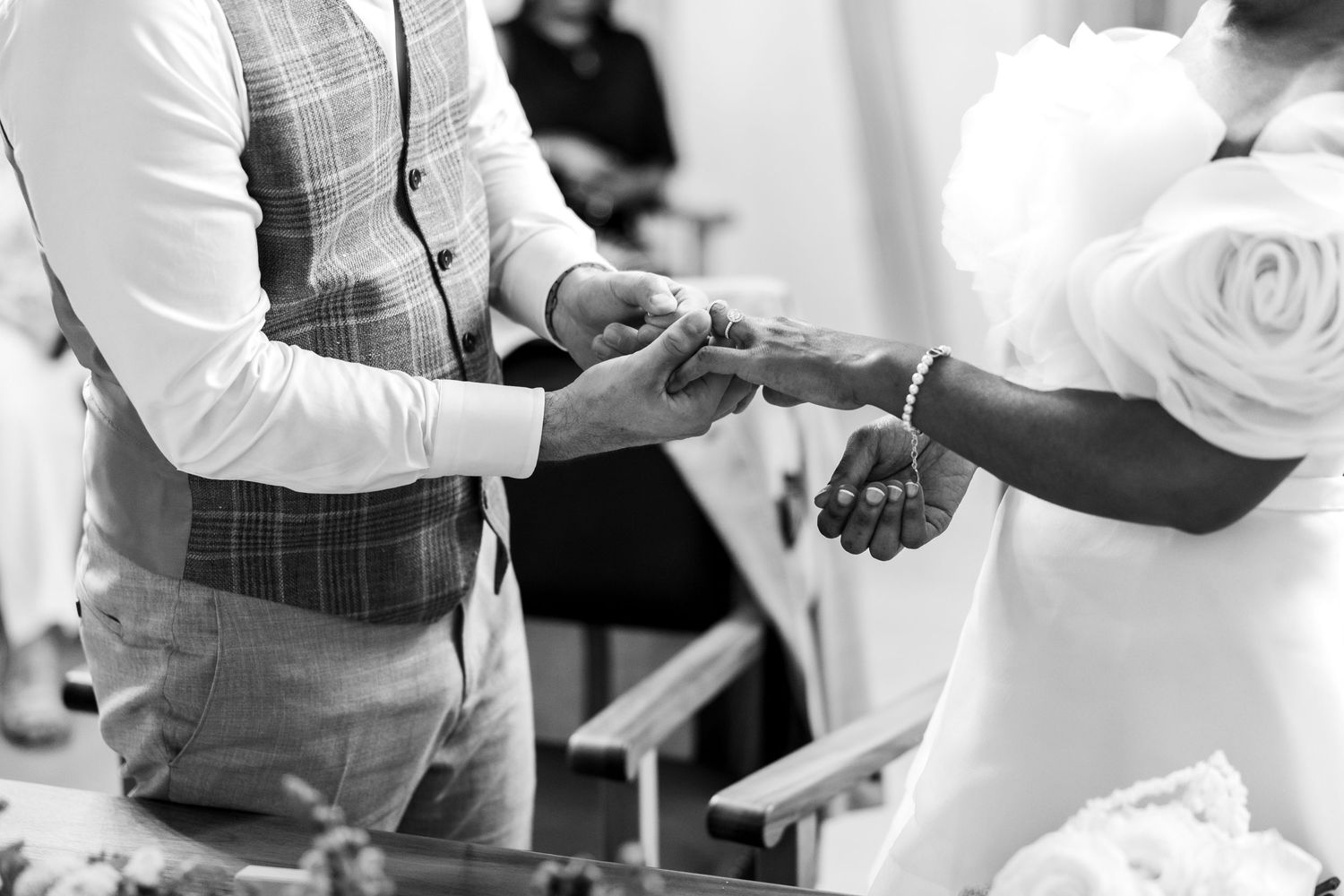 Close-up black and white photo of groom sliding wedding ring onto brides hand at ceremony.