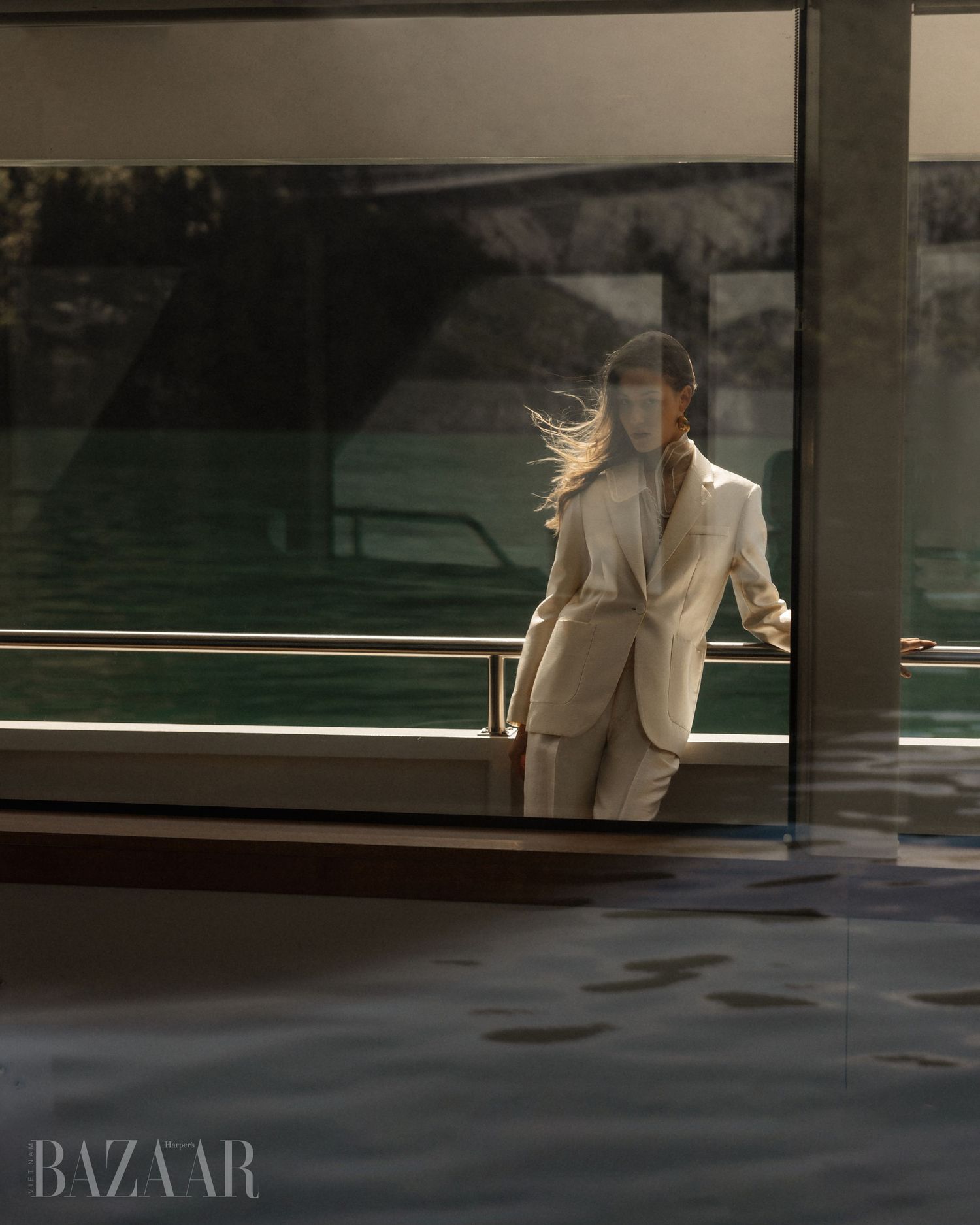 Woman in cream pantsuit walks through golden light near glass walls on a luxury vessel.