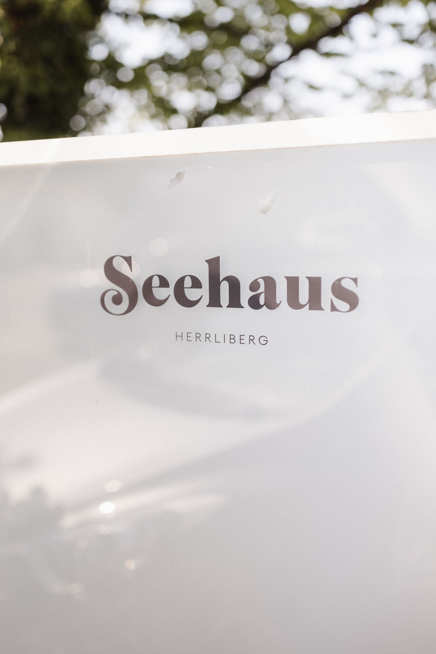 Elegant white sign for Seehaus Herrliberg venue with stylish serif typography outdoors.
