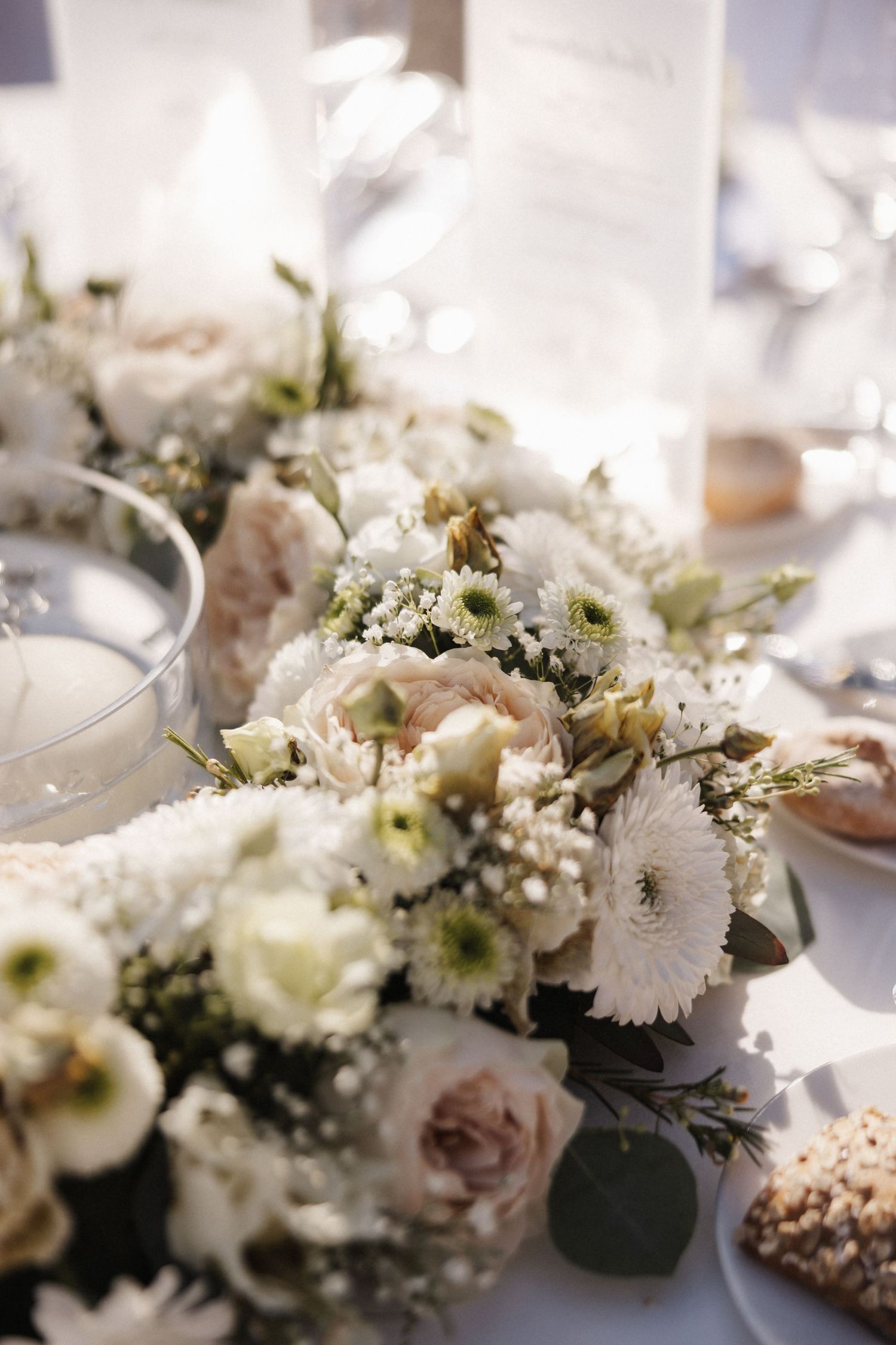Lush wedding table floral arrangement featuring white gerberas, blush roses, and baby's breath.