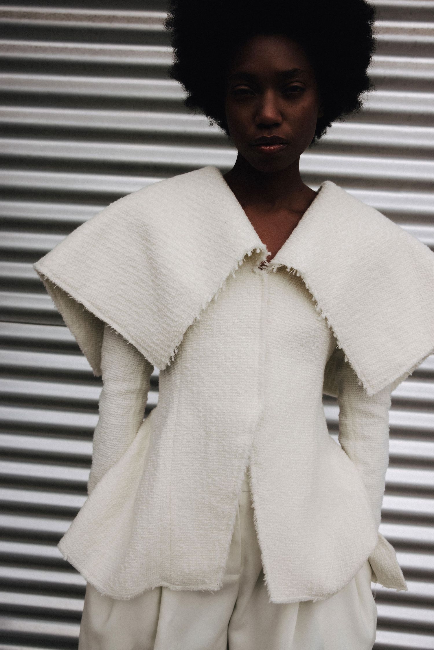 Front view of model in a white boucle oversized collar vest with frayed edges over a white ensemble.